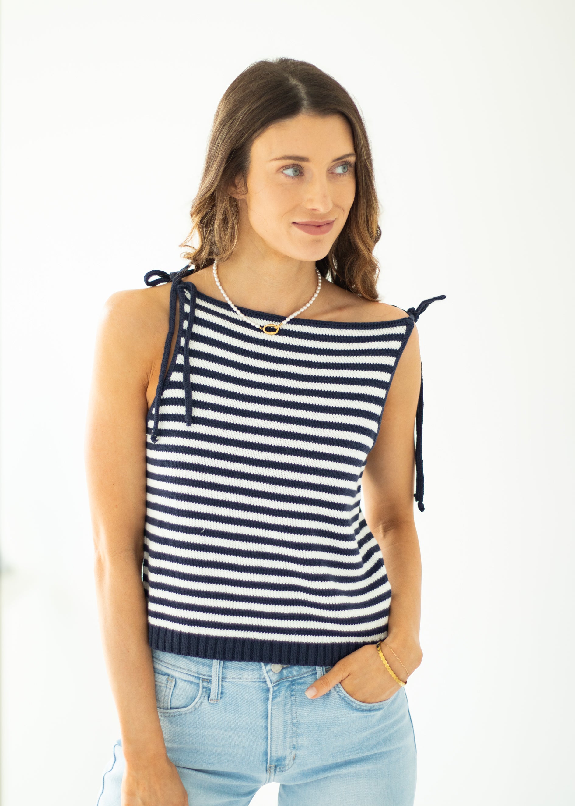 Woman wearing a navy and white striped sleeveless top with light blue jeans on a white background