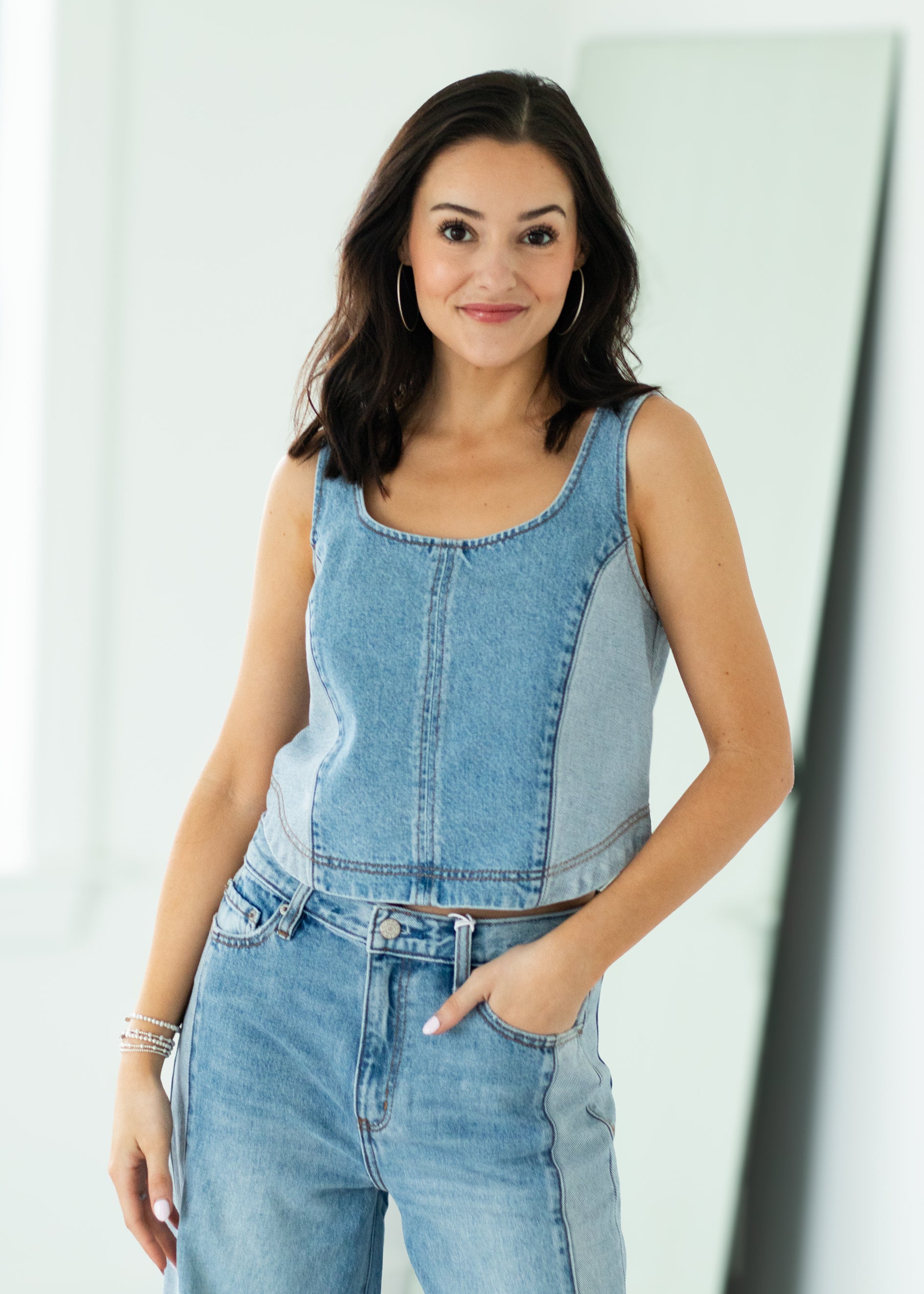 Woman wearing a denim sleeveless top and jeans against a white background