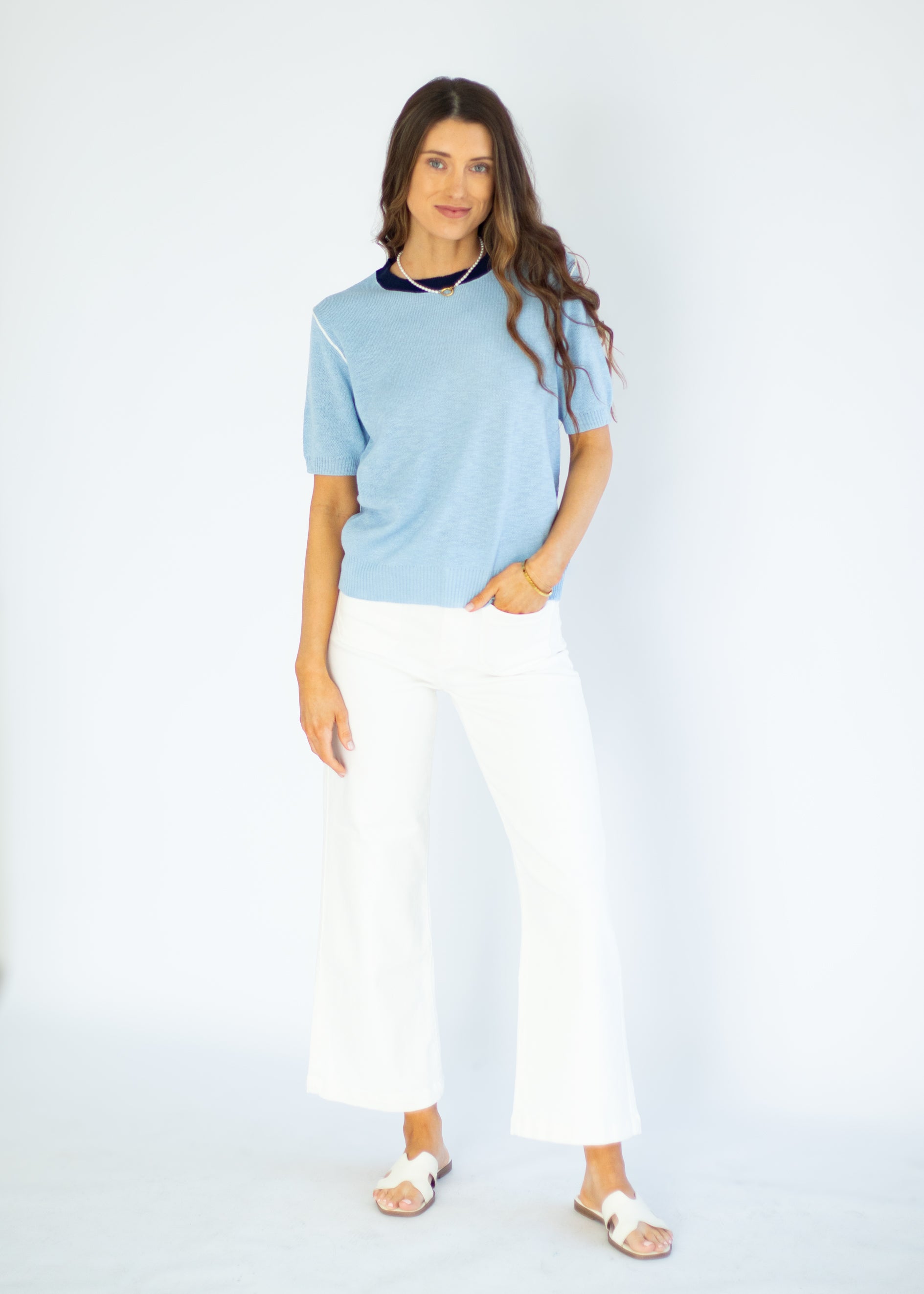 Woman wearing a light blue sweater and white pants on a white background
