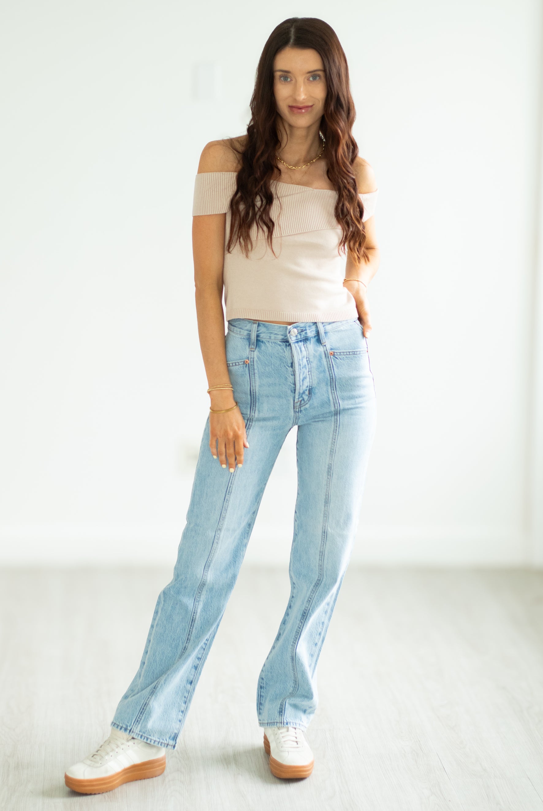 Woman wearing a beige top and light blue jeans on a white background