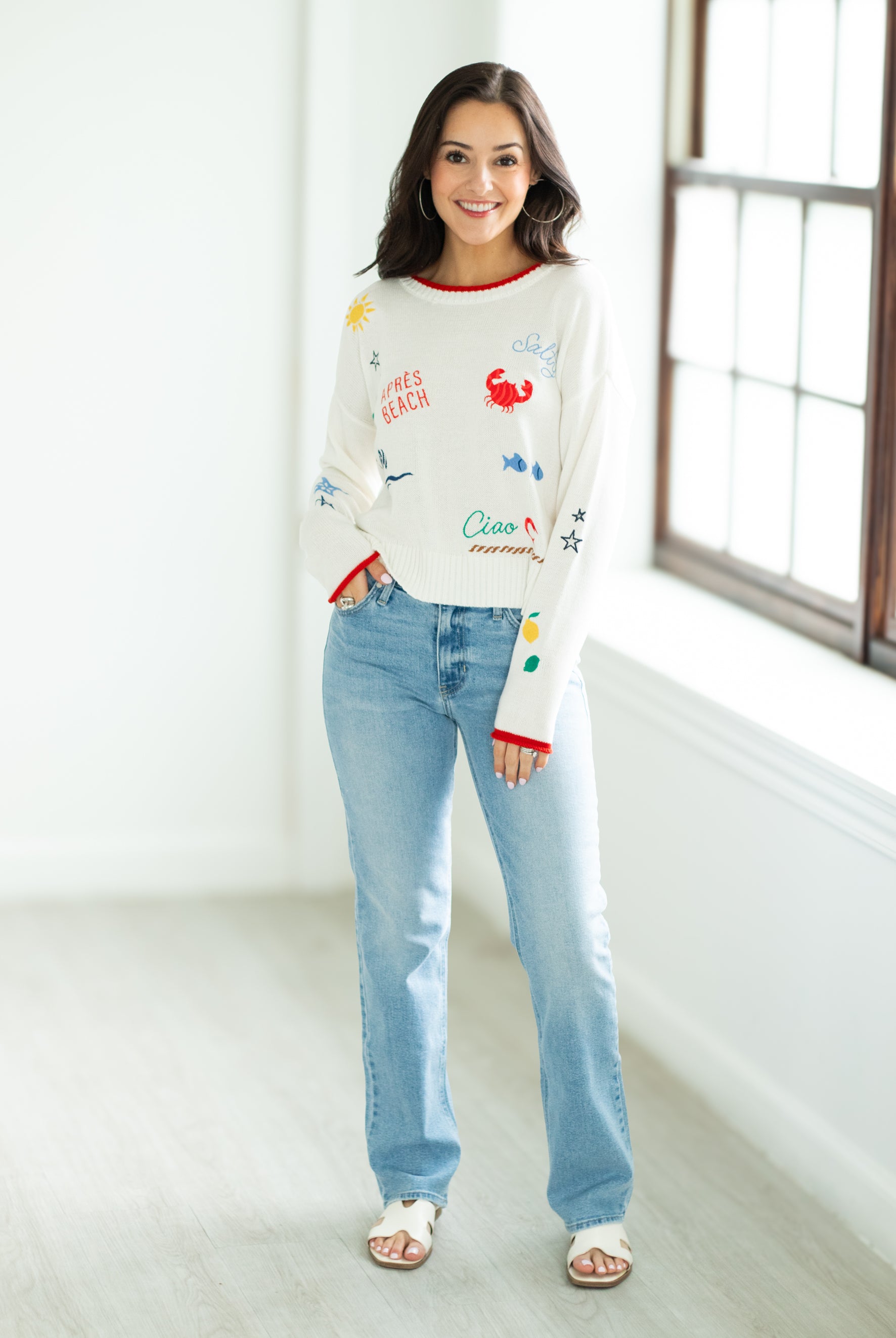 Woman wearing a colorful sweater and light blue jeans indoors.