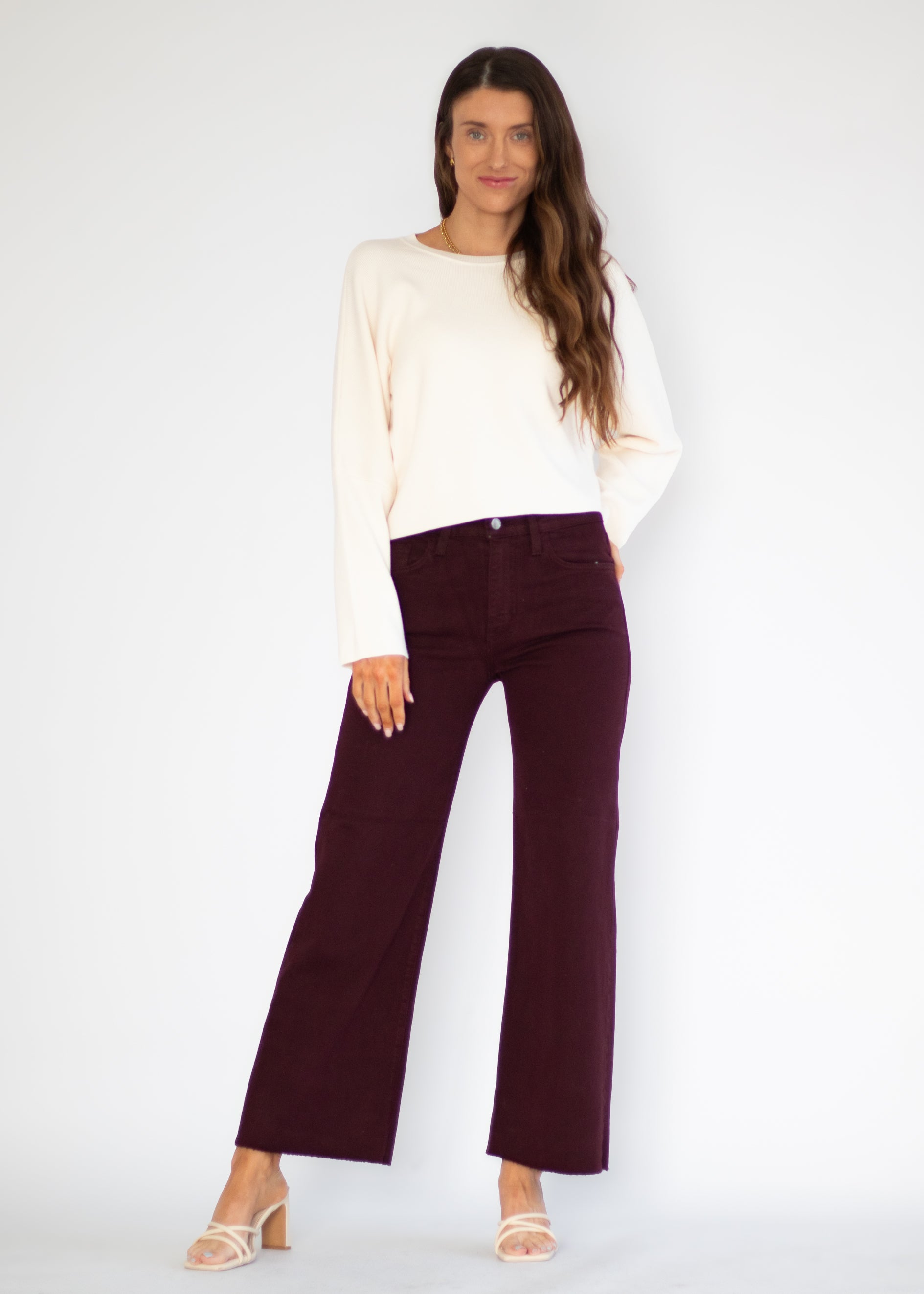 A woman modeling a cream long-sleeve knit top and dark burgundy wide-leg cropped pants against a plain white studio background.