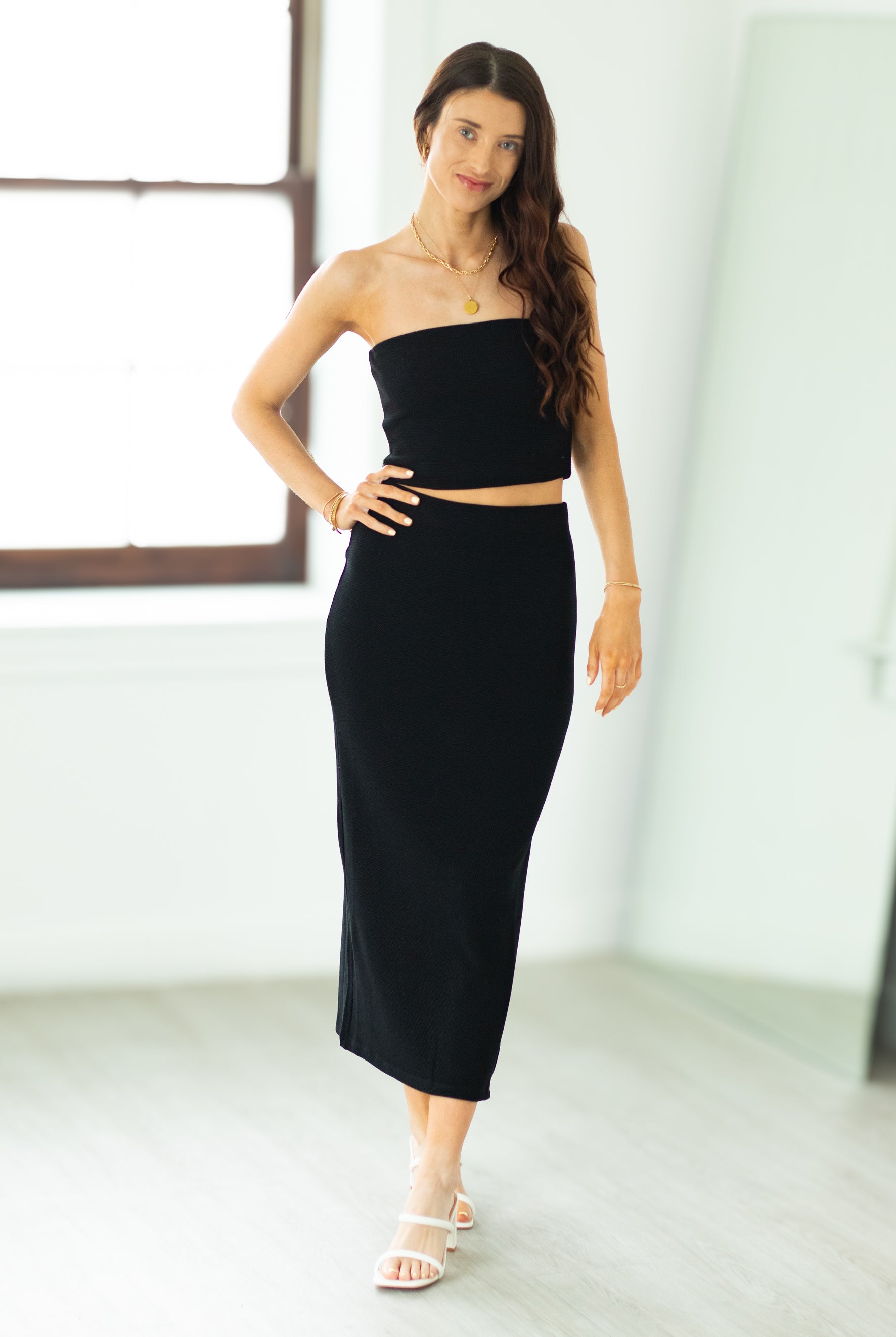 Woman wearing a black strapless top and high-waisted skirt in a minimalistic room.
