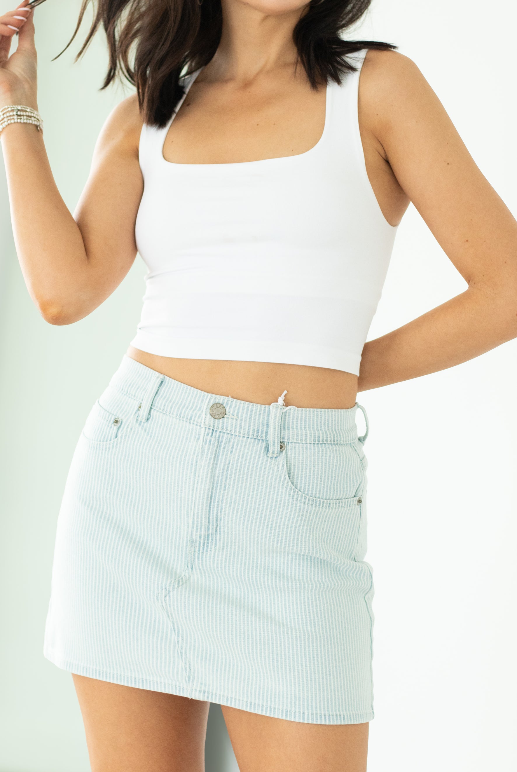 Woman wearing a white tank top and light blue checkered skirt on a plain background