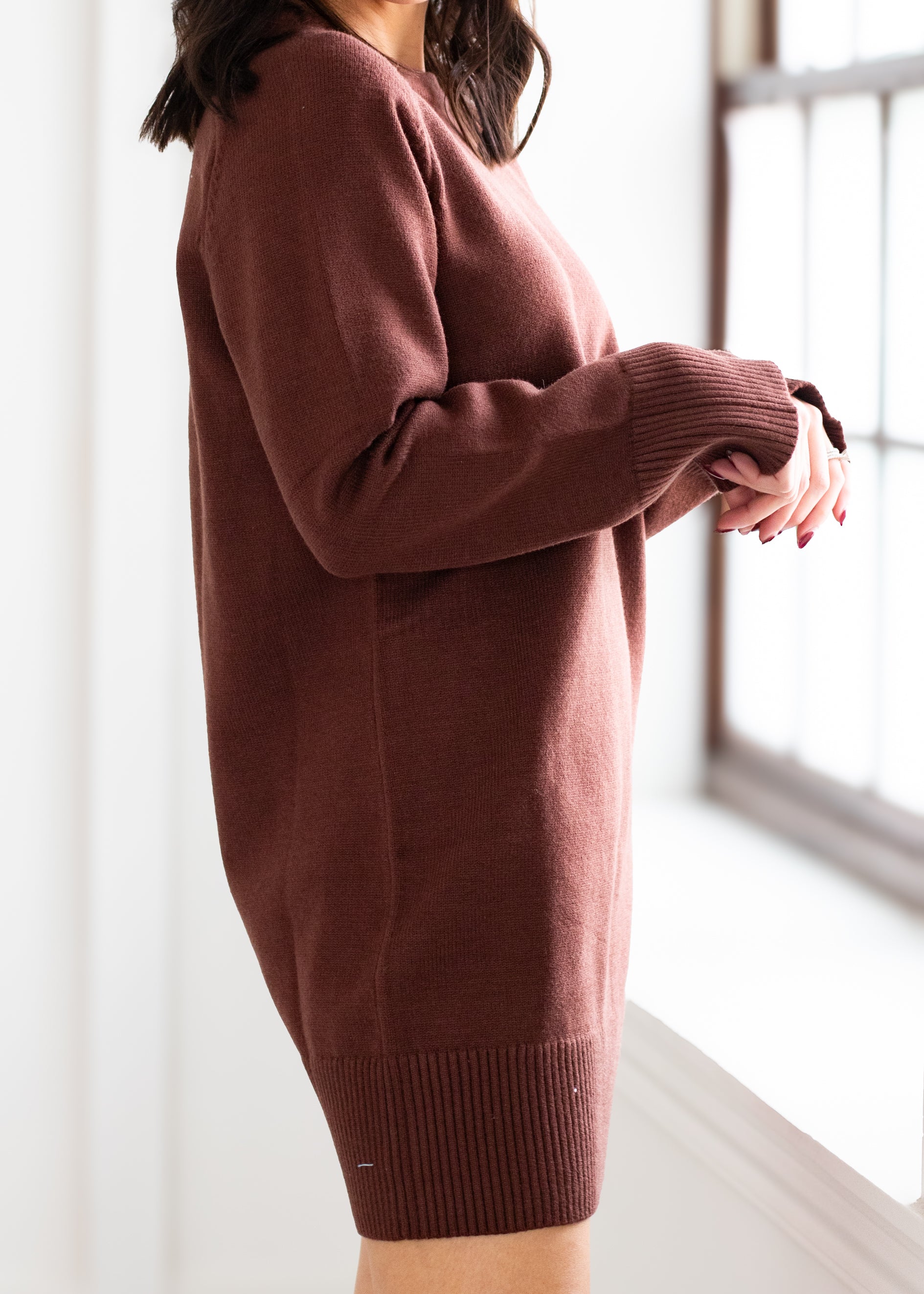 Person wearing a brown sweater in a bright room with a window.