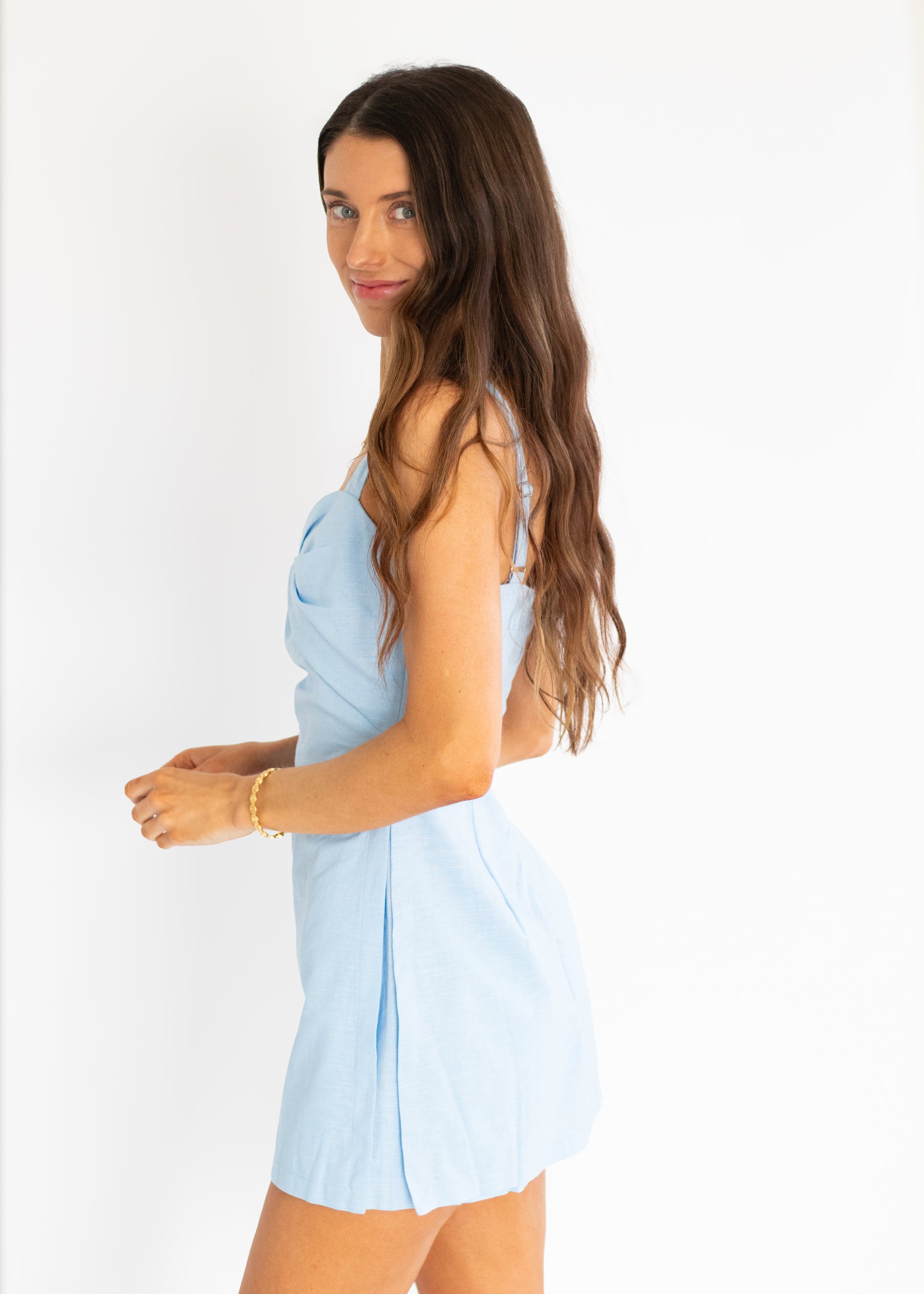 A woman with long brown hair models a light blue sleeveless romper against a plain white background.