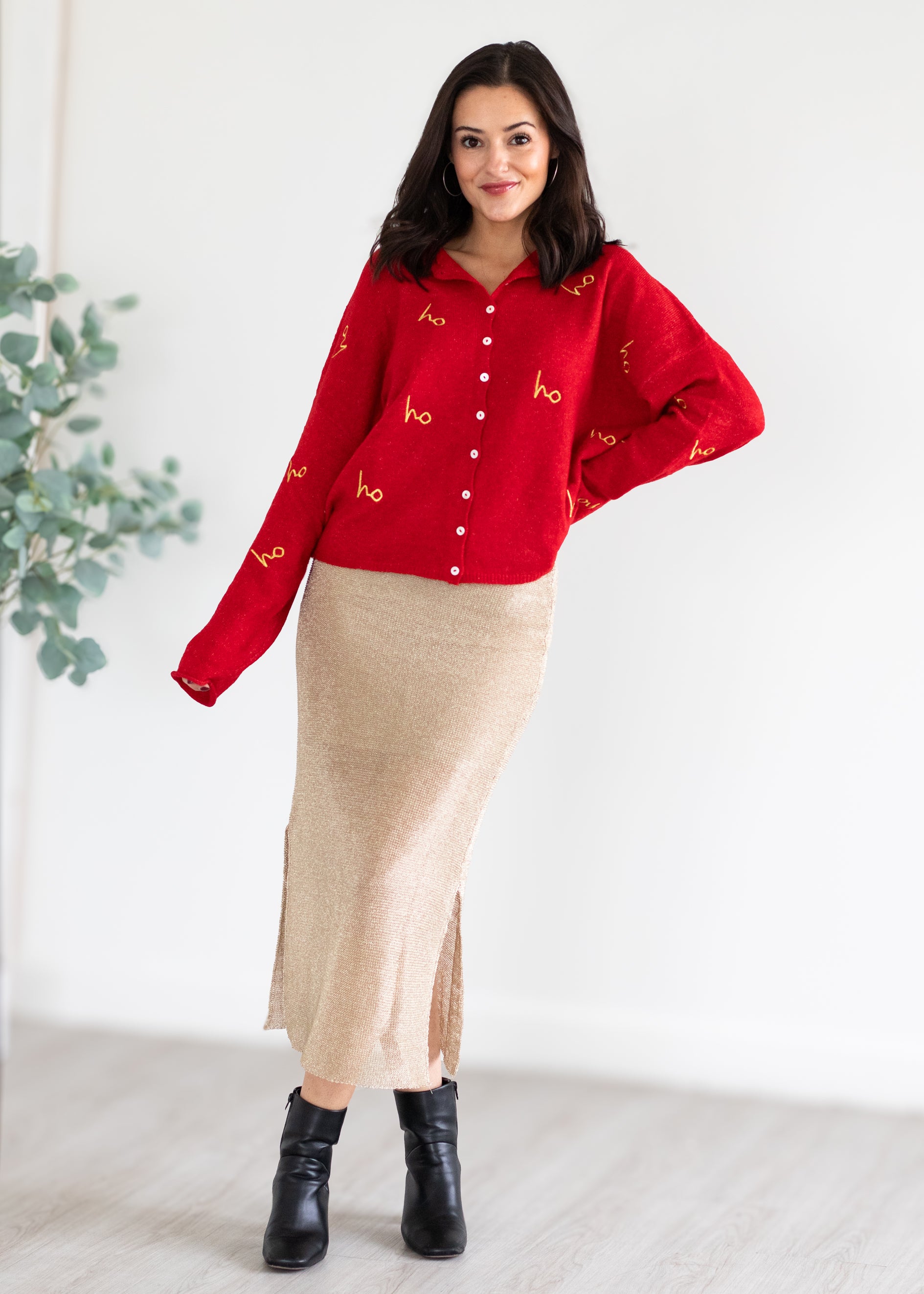 Woman wearing a red sweater with gold text and a gold metallic skirt indoors.