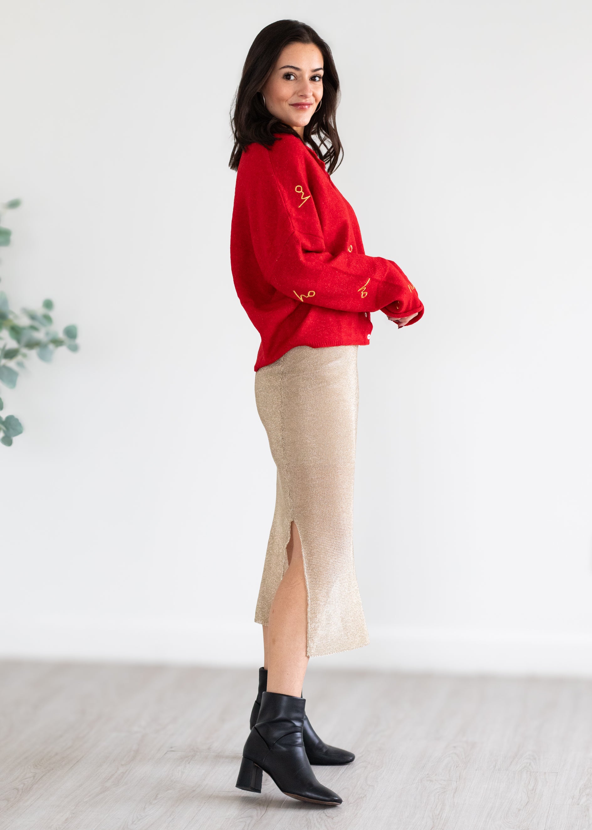 Woman wearing a red sweater and gold skirt with black boots on a white background