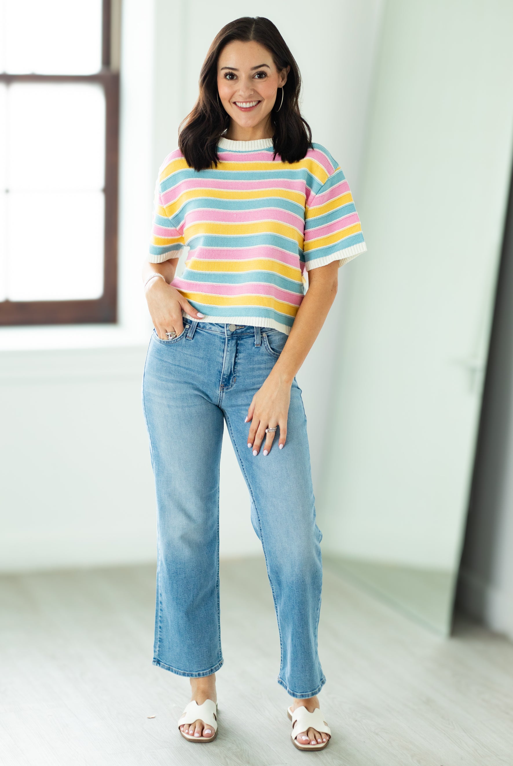 Woman wearing a colorful striped shirt and blue jeans indoors.