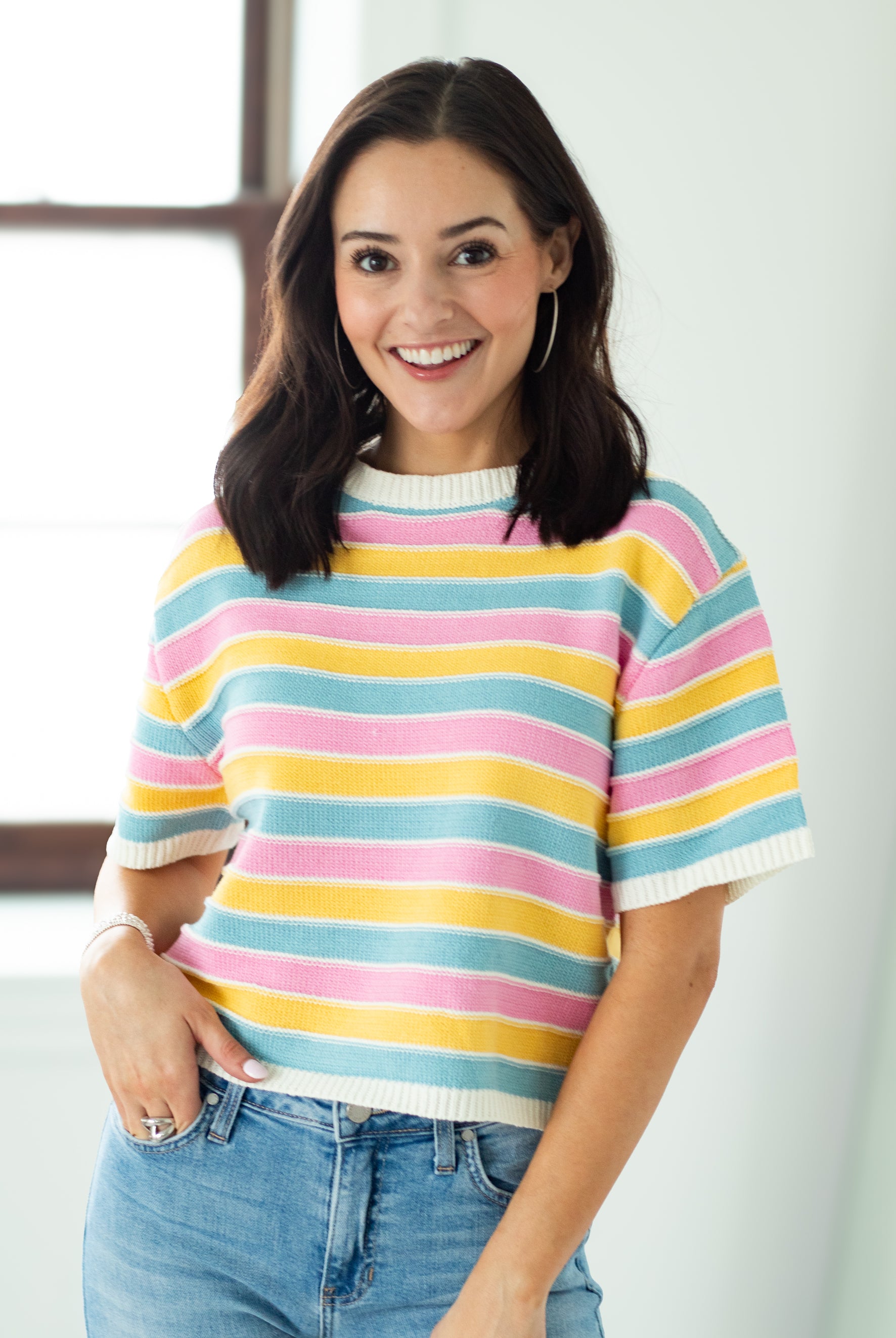 Woman wearing a colorful striped sweater and jeans indoors.