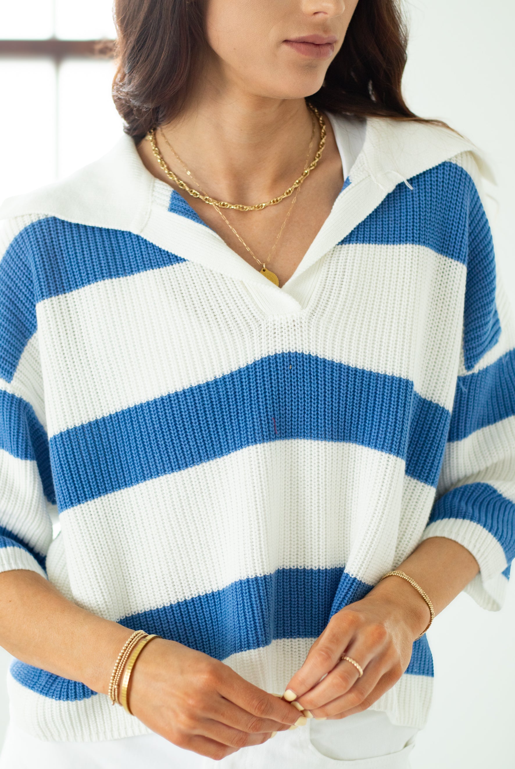Person wearing a blue and white striped sweater with gold jewelry.
