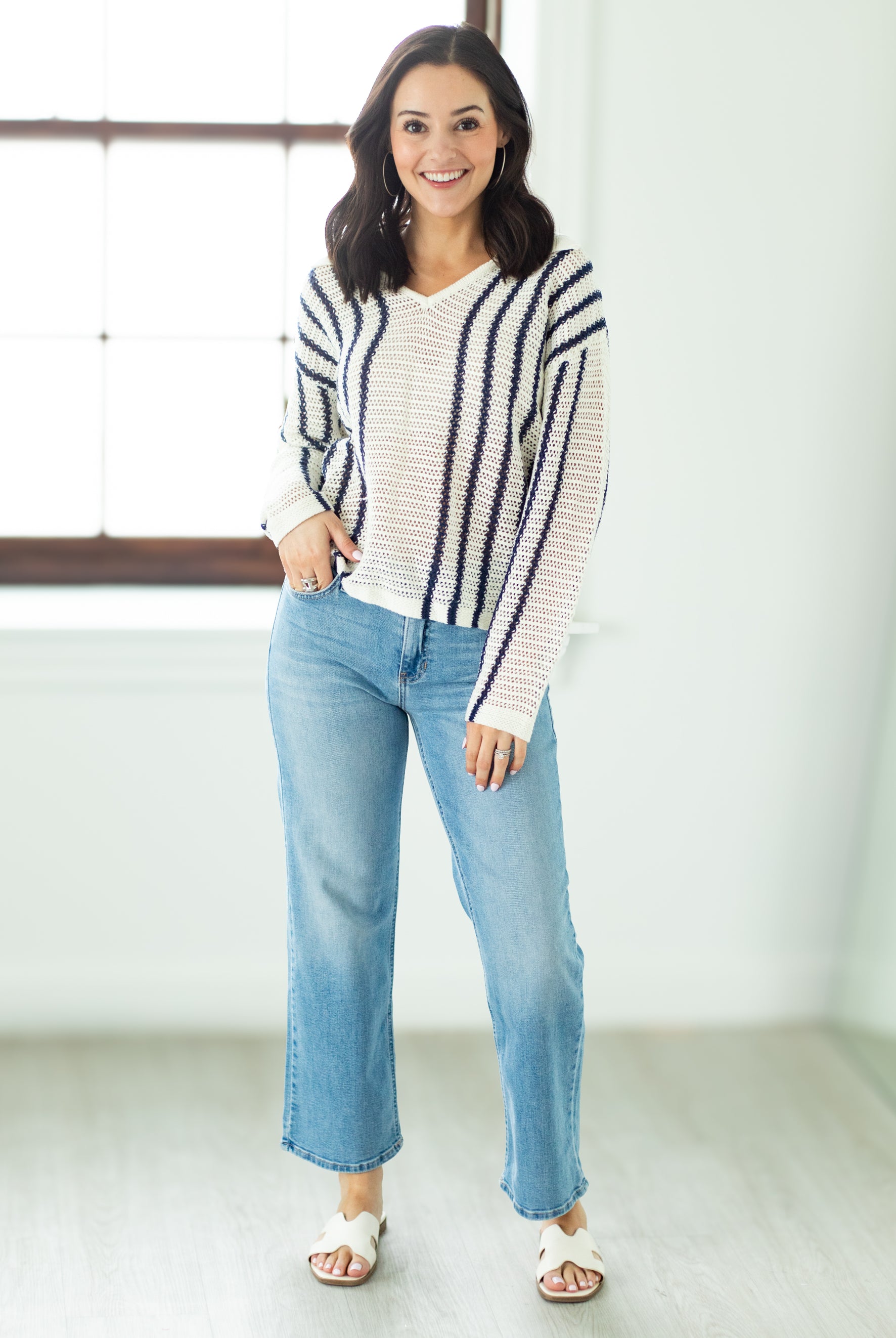 Woman wearing a striped sweater and blue jeans standing indoors.