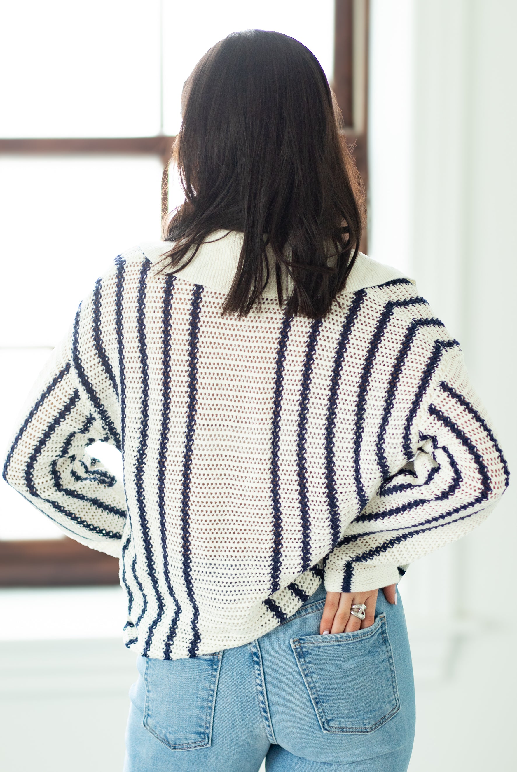 Person wearing a striped sweater and blue jeans in a room with a window.