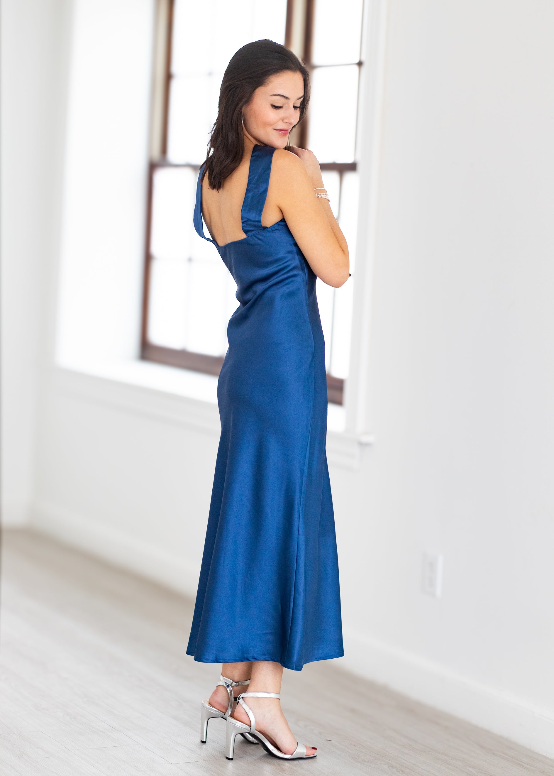 Woman wearing a blue dress in a bright room with large windows.