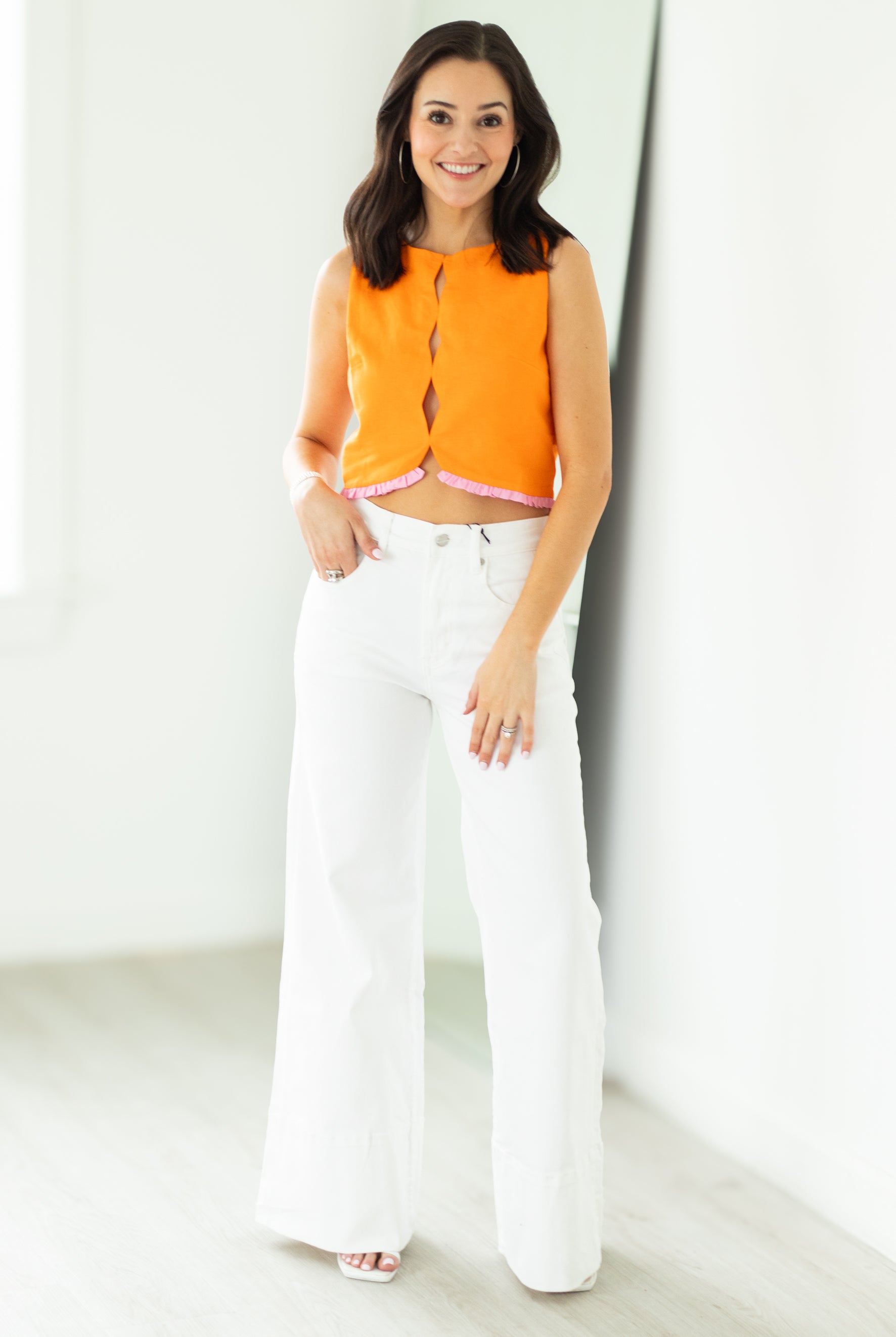 Woman wearing an orange top and white pants against a white background