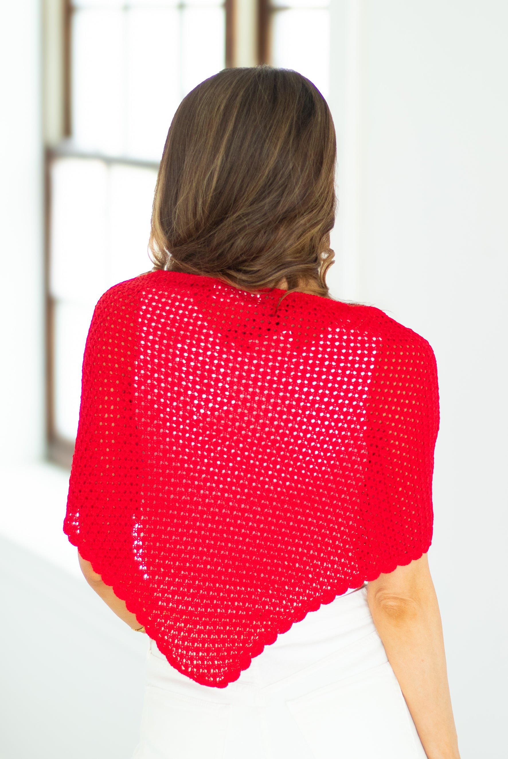 Person wearing a bright red knitted shawl against a white background
