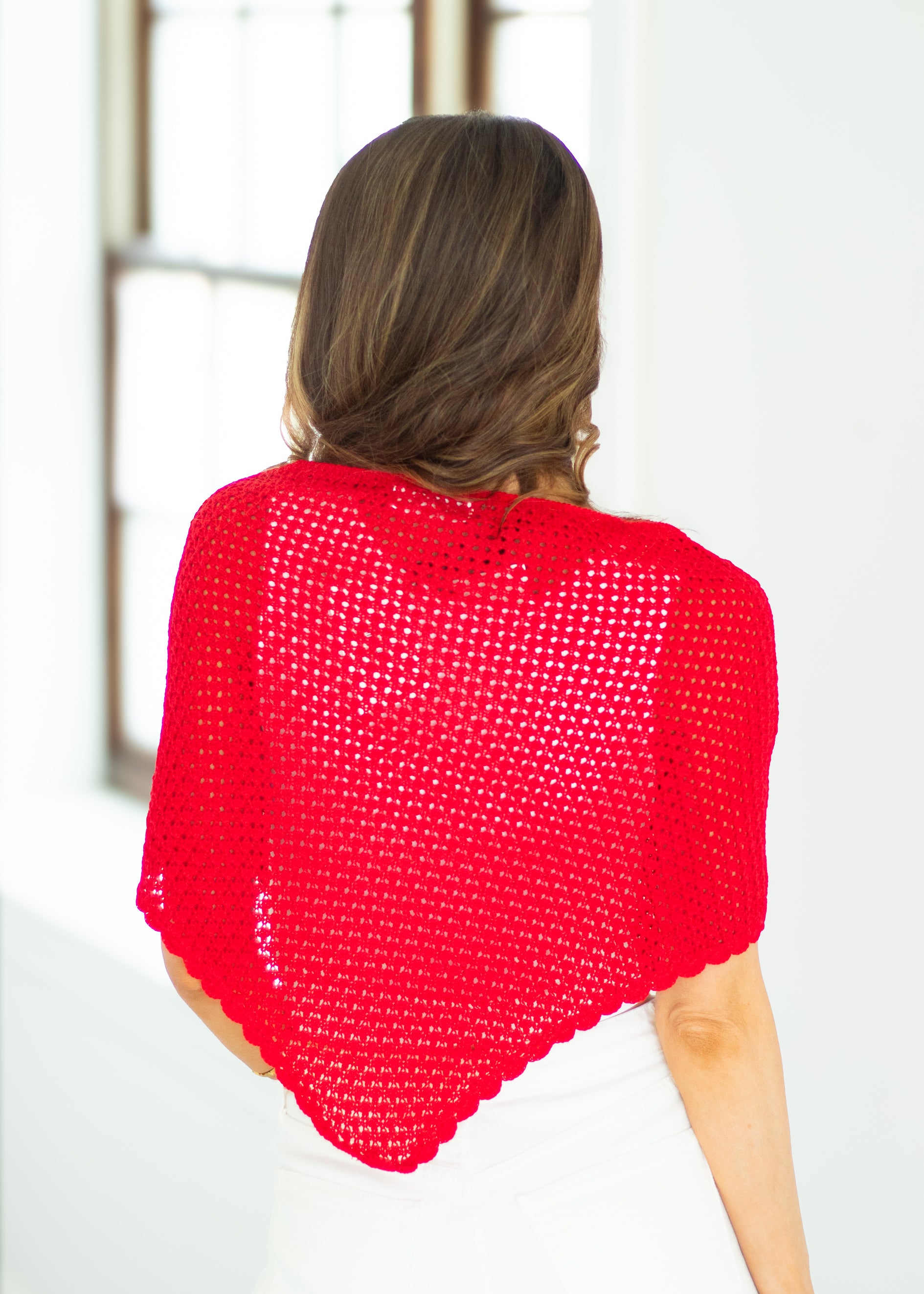 Person wearing a bright red knitted shawl against a white background