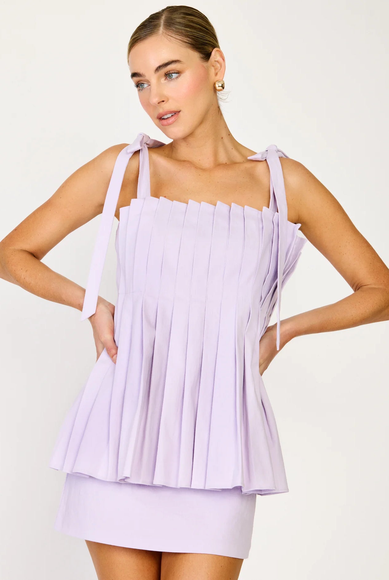 Woman wearing a light purple pleated dress against a white background