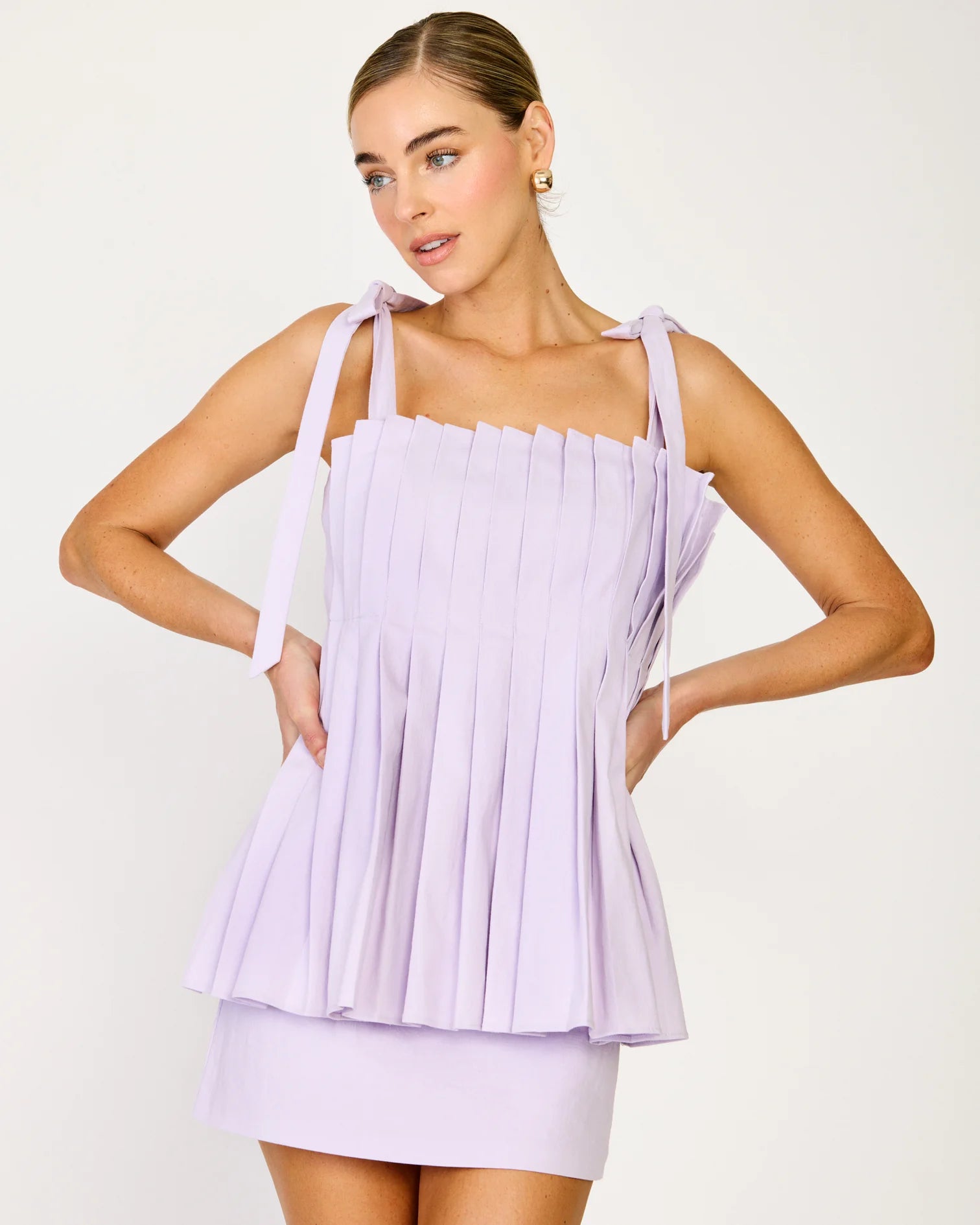 Woman wearing a light purple pleated dress against a white background