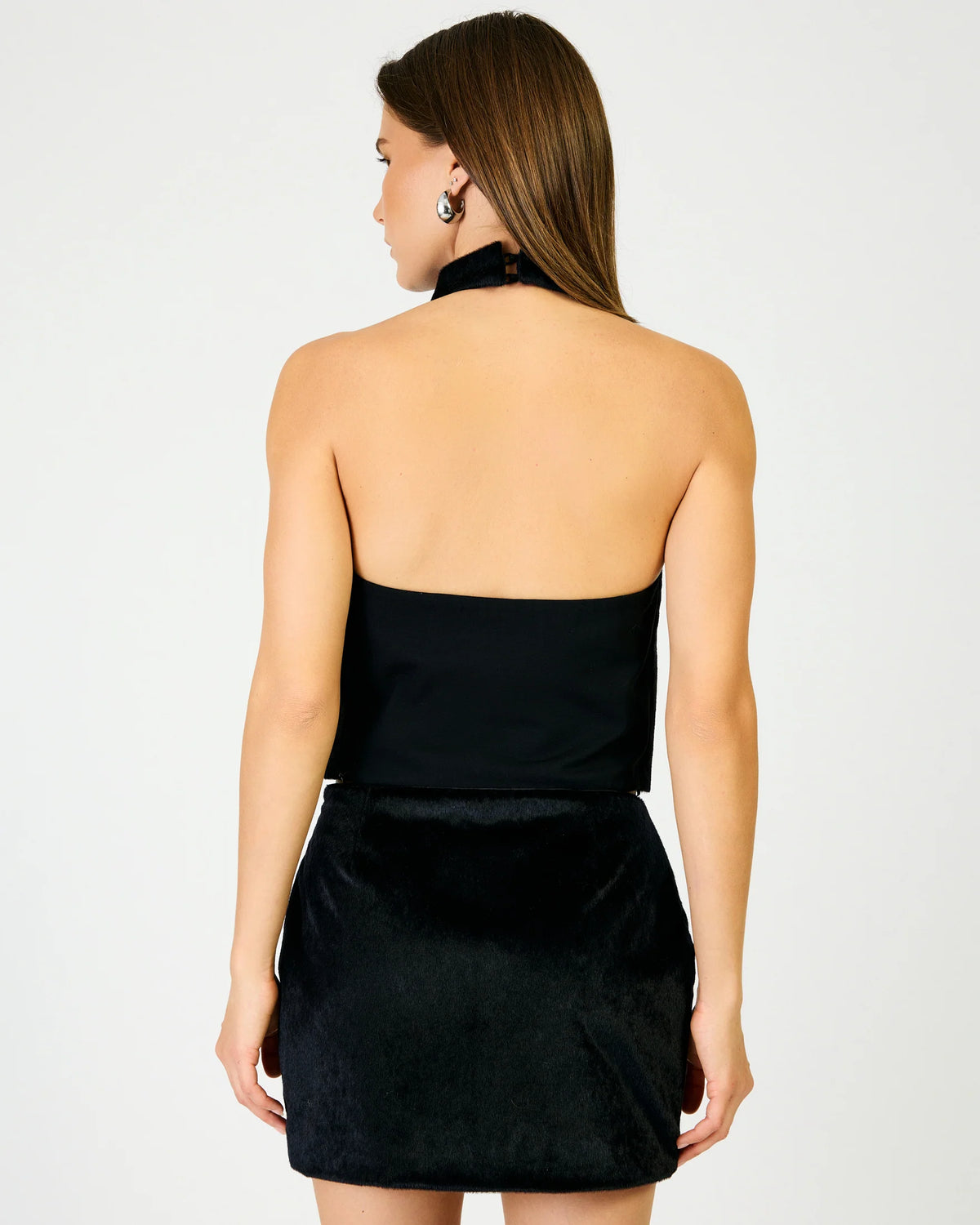 A woman shown from the back wearing a black top against a grey wall