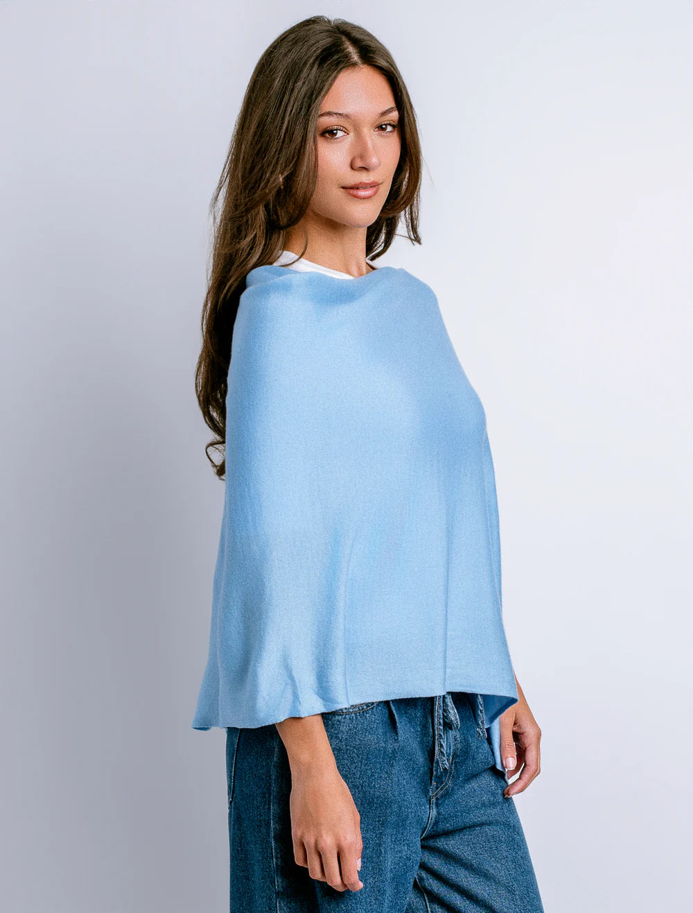 Woman wearing a light blue poncho over a white shirt with jeans on a plain background
