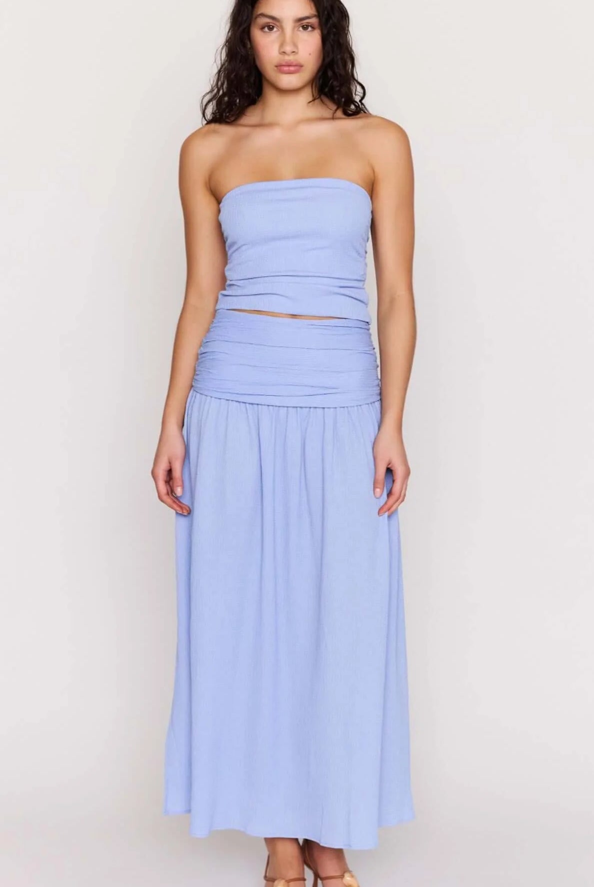 Woman wearing a light blue strapless top and skirt in a bright room.