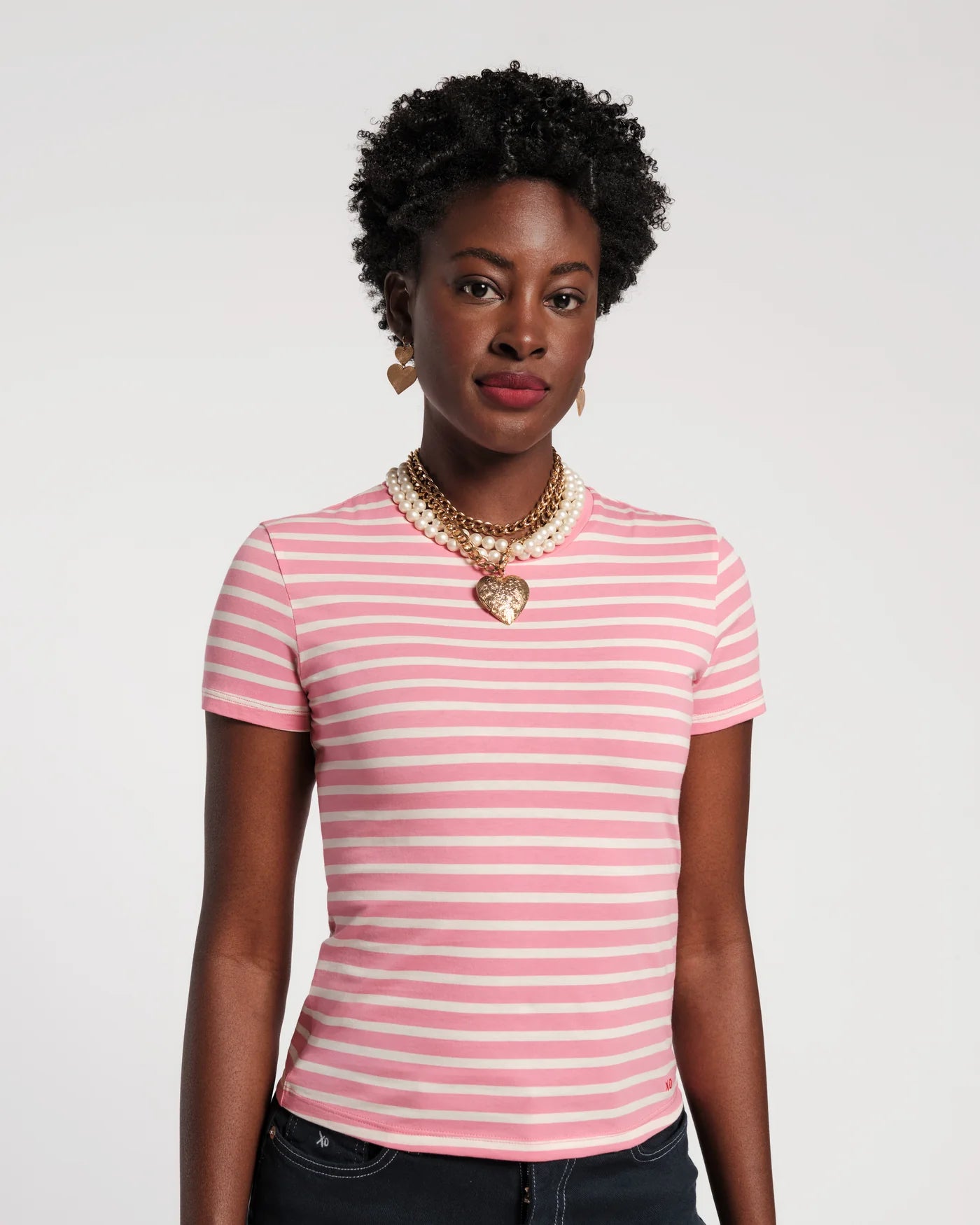 Woman wearing a pink and white striped shirt with a necklace on a plain background