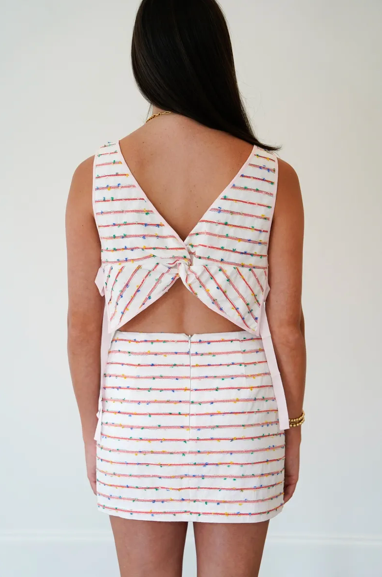 Woman wearing a striped dress with a unique back design on a plain background