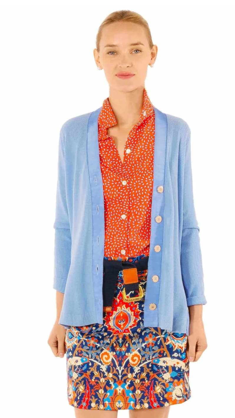 Woman wearing a blue cardigan over a patterned shirt and skirt on a white background