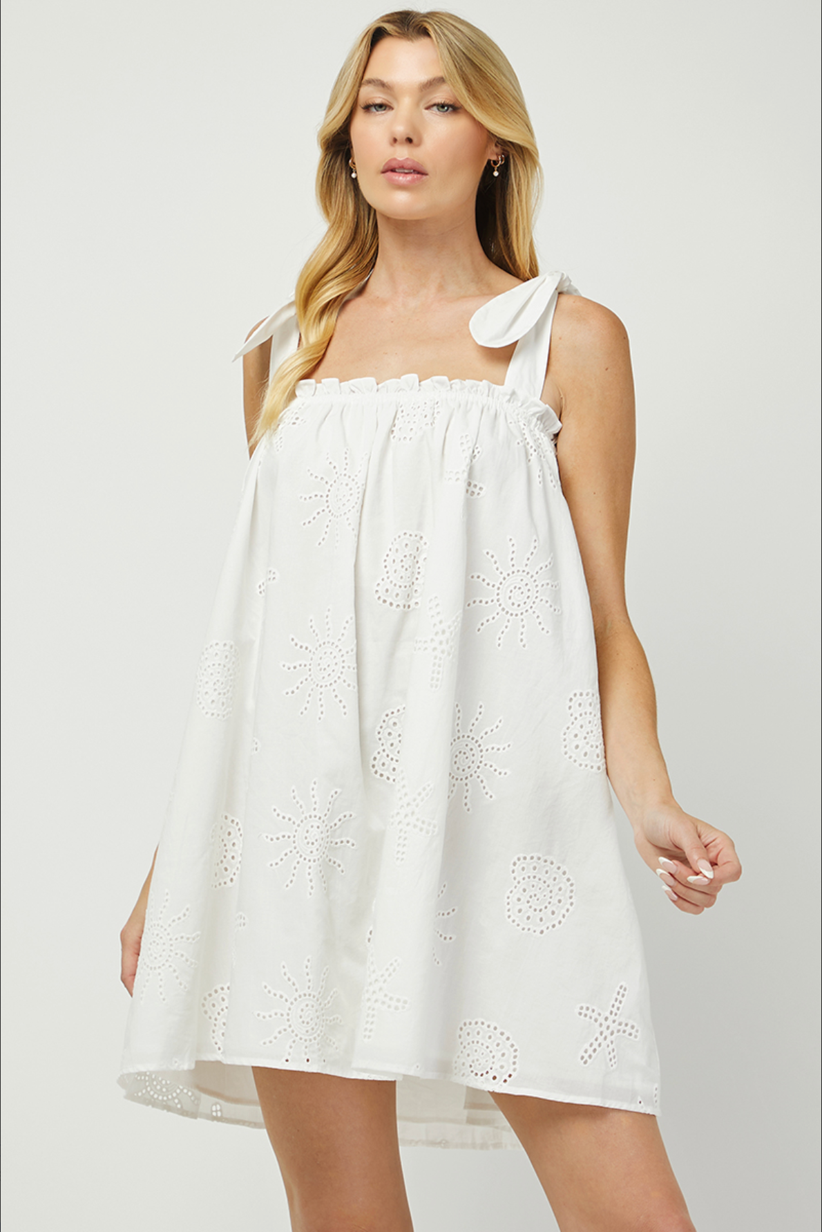 Woman wearing a white dress with floral embroidery on a plain background
