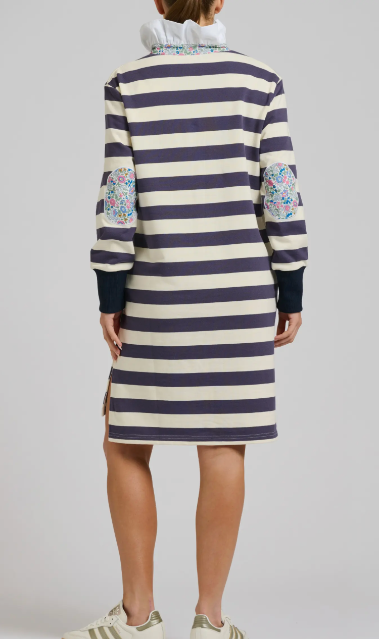 Person wearing a striped dress with floral patterns on sleeves against a plain background