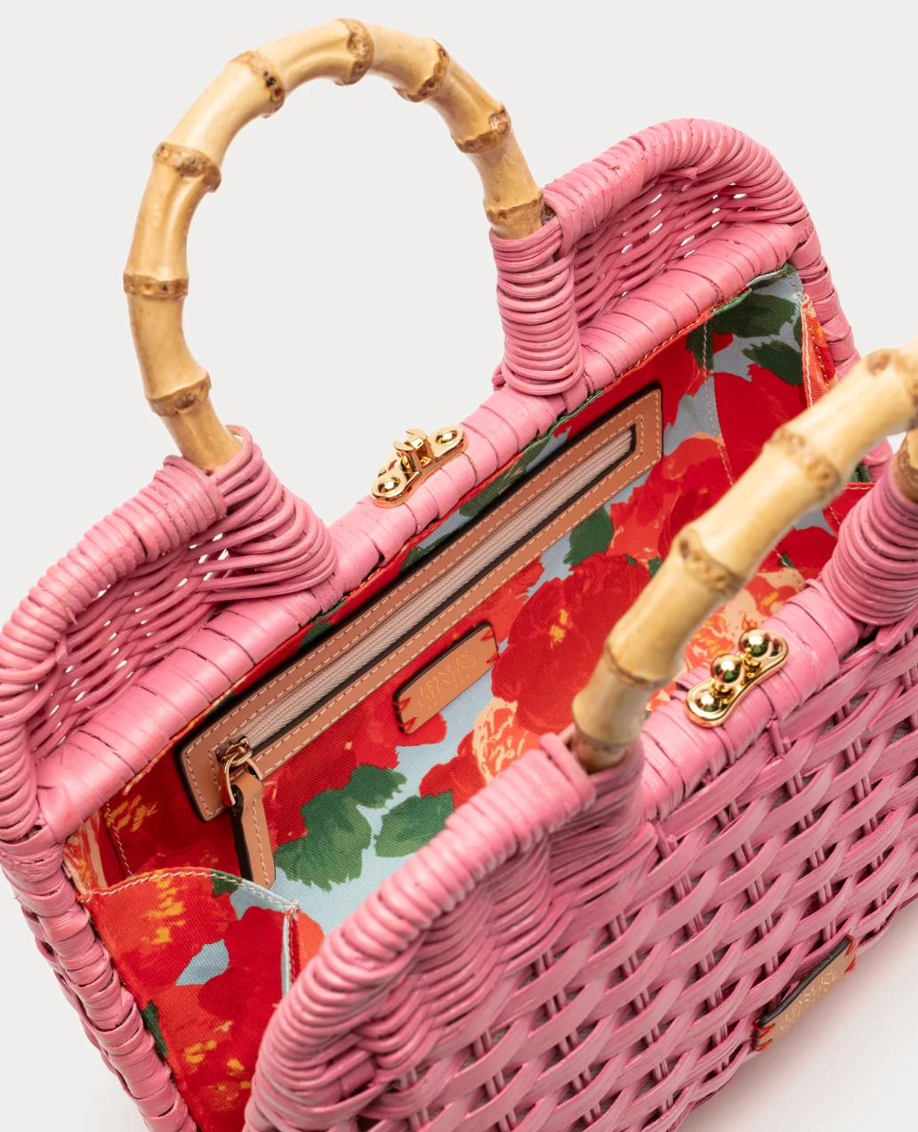 Pink woven handbag with floral pattern and bamboo handles on a white background