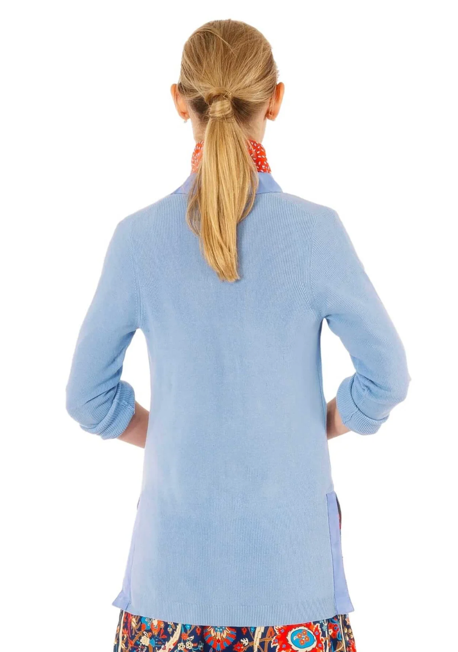 Person wearing a light blue cardigan with a floral patterned bottom on a white background
