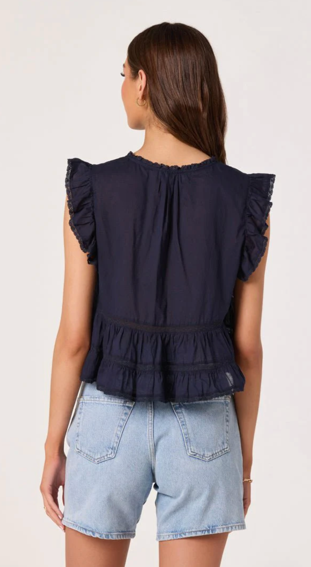 Woman wearing a navy blue top with ruffled sleeves and denim shorts on a white background