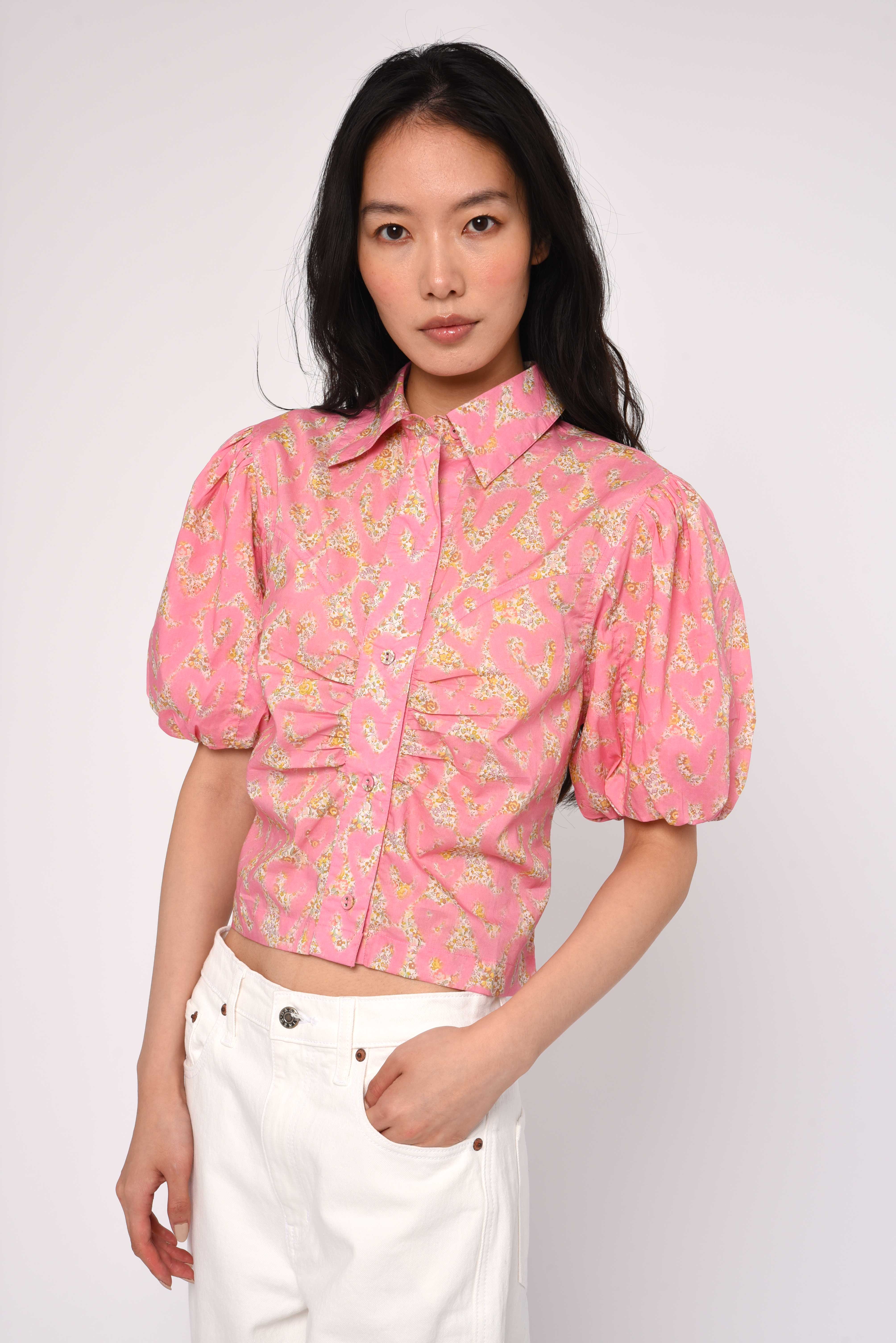 Woman wearing a pink floral blouse with white pants on a plain background