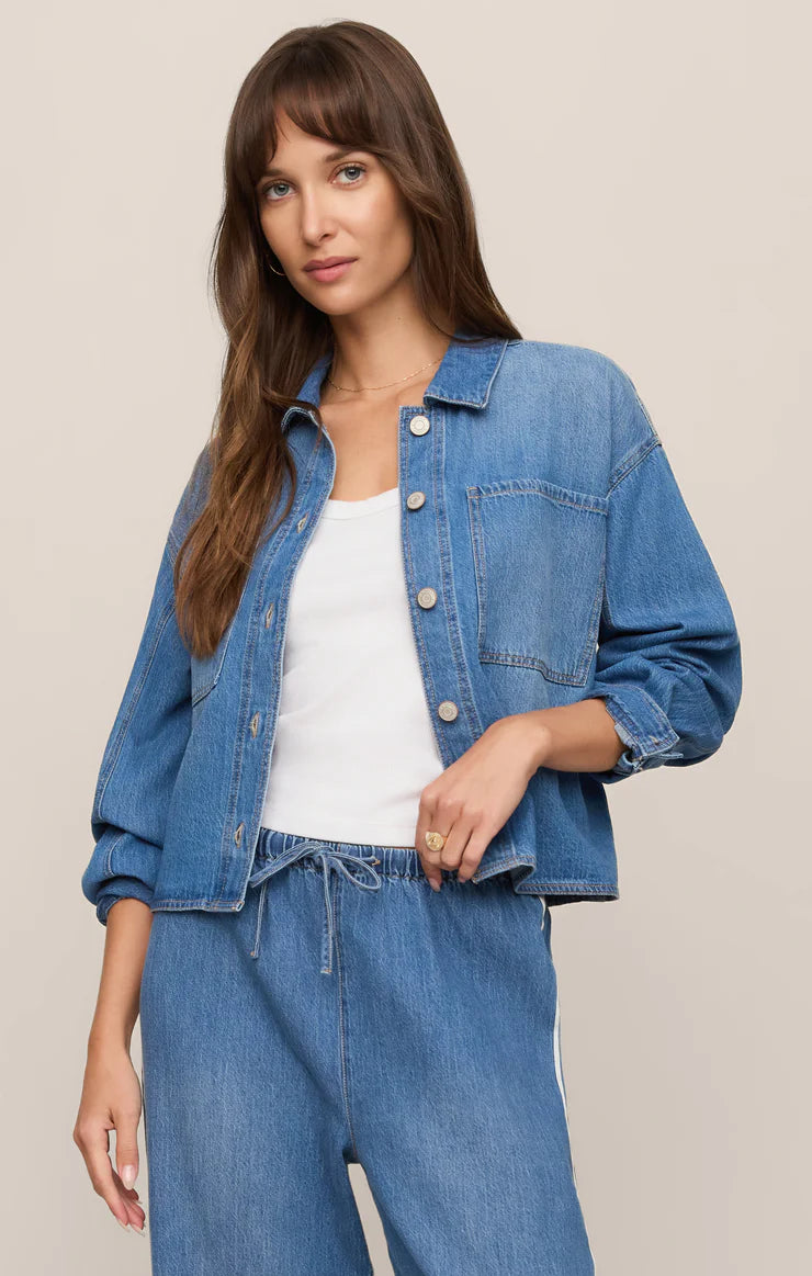 Woman wearing a blue denim jacket and pants on a beige background