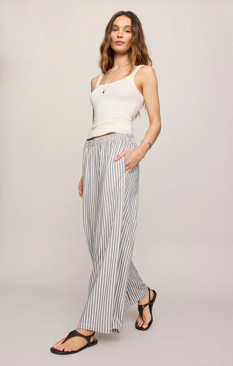 Woman wearing a white sleeveless top and striped pants on a plain background