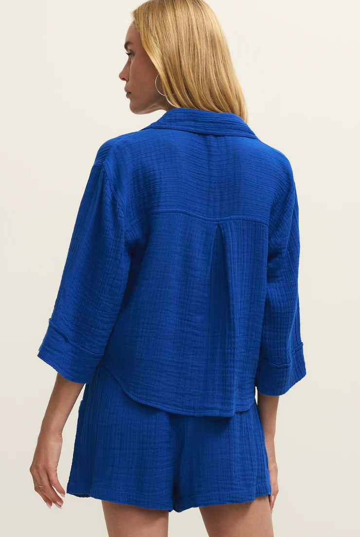 Woman wearing a blue textured outfit with a jacket and shorts on a beige background