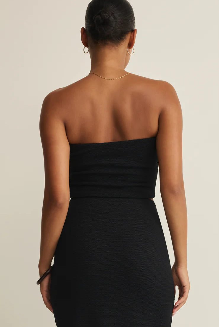 Woman wearing a black strapless dress against a beige background