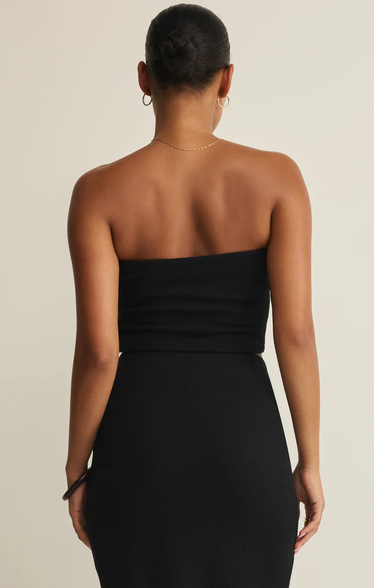 Woman wearing a black strapless dress against a beige background