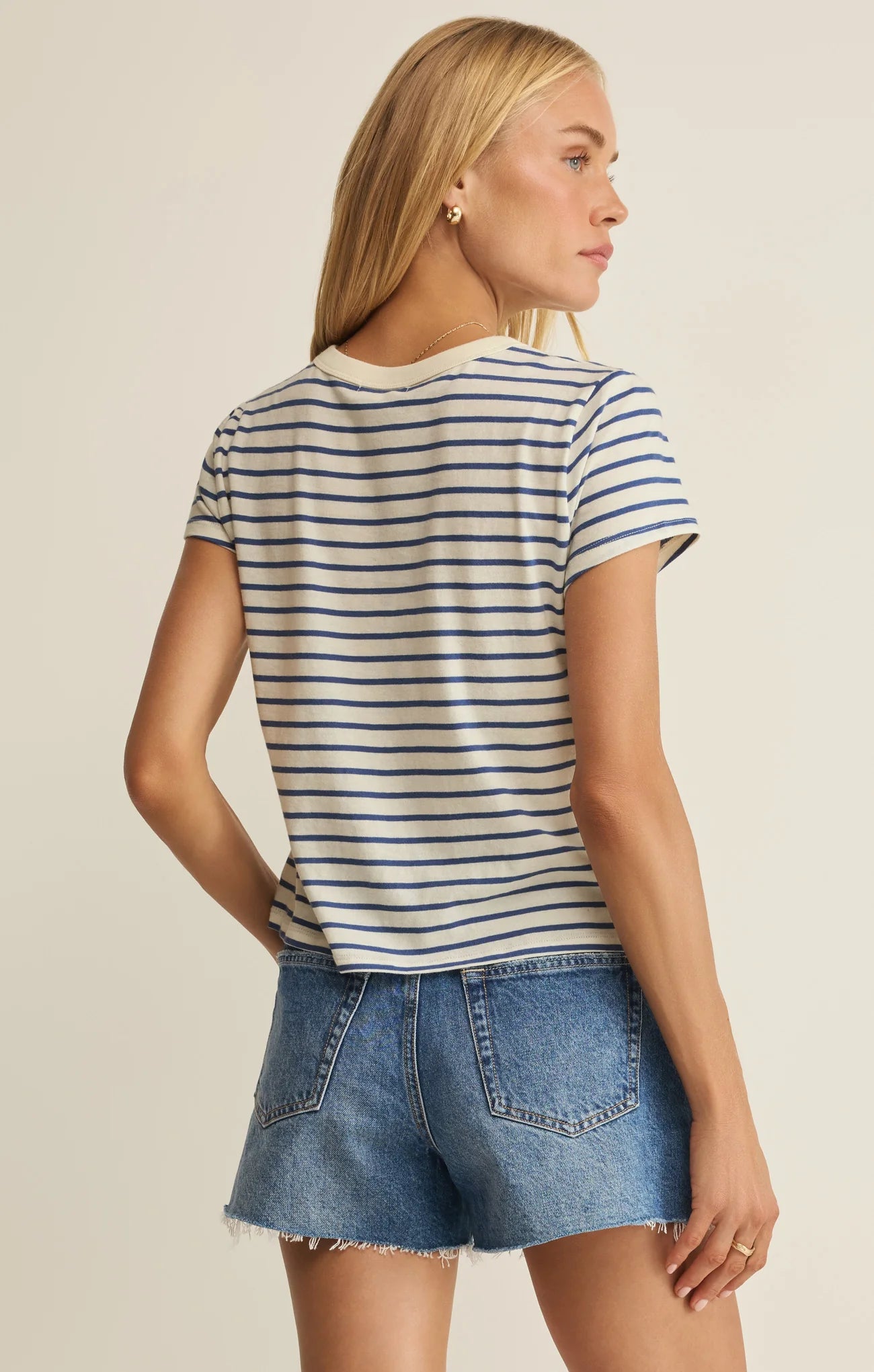 Woman wearing a striped shirt and denim shorts on a beige background