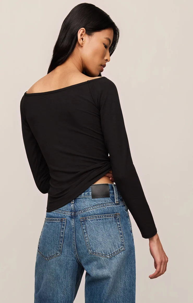 Woman wearing a black long-sleeve top and blue jeans on a beige background
