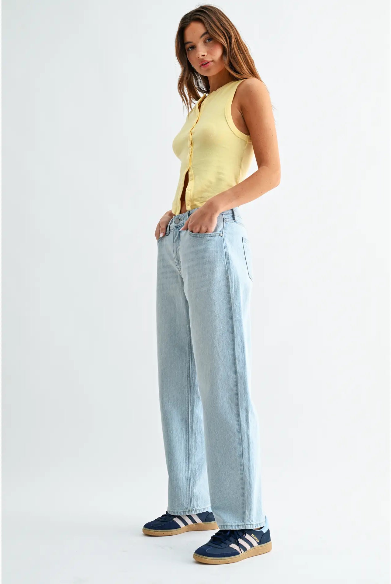 Woman wearing a yellow sleeveless top and light blue jeans on a white background