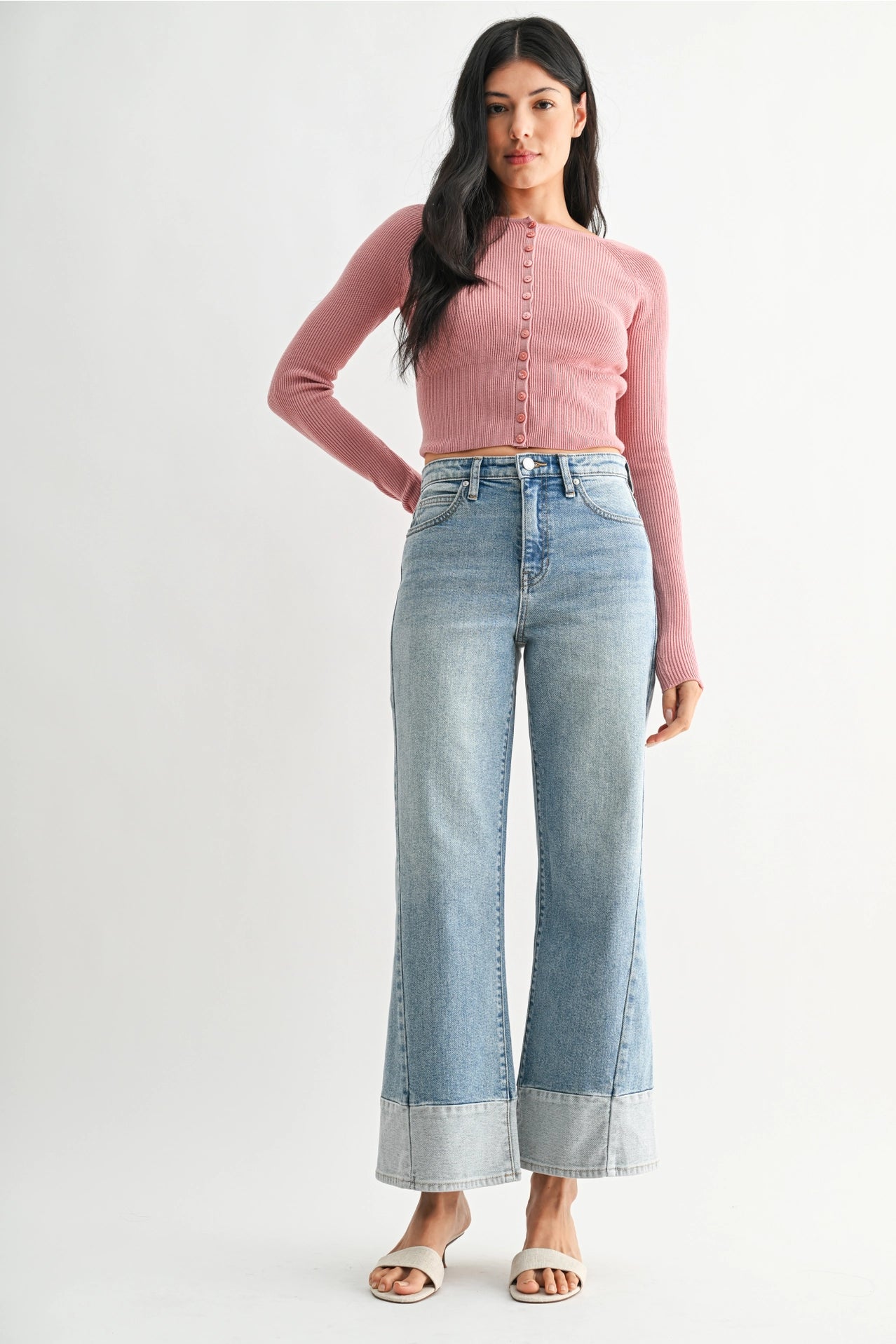 Woman wearing a pink long-sleeve top and light blue jeans on a white background