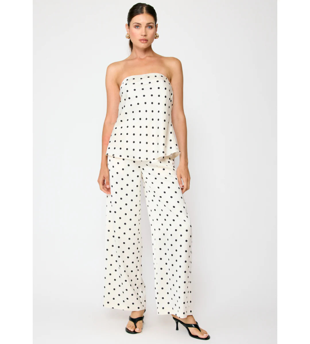 Woman wearing a strapless polka dot top and wide-leg pants on a white background