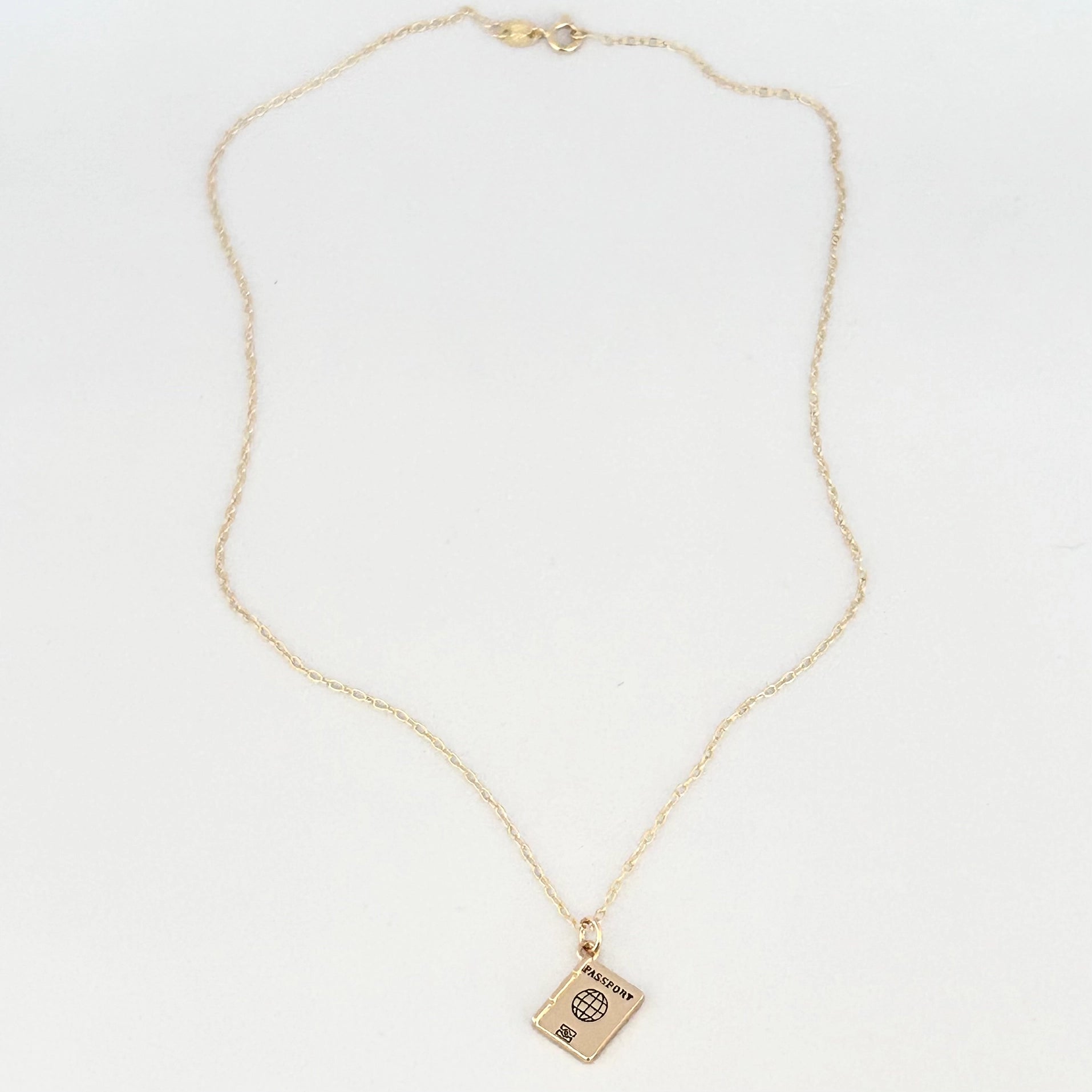 A delicate gold chain necklace with a small rectangular pendant featuring a passport cover