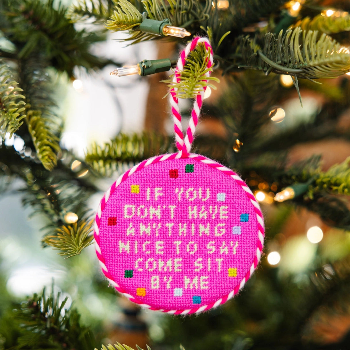 Pink needlepoint ornament with text on a Christmas tree