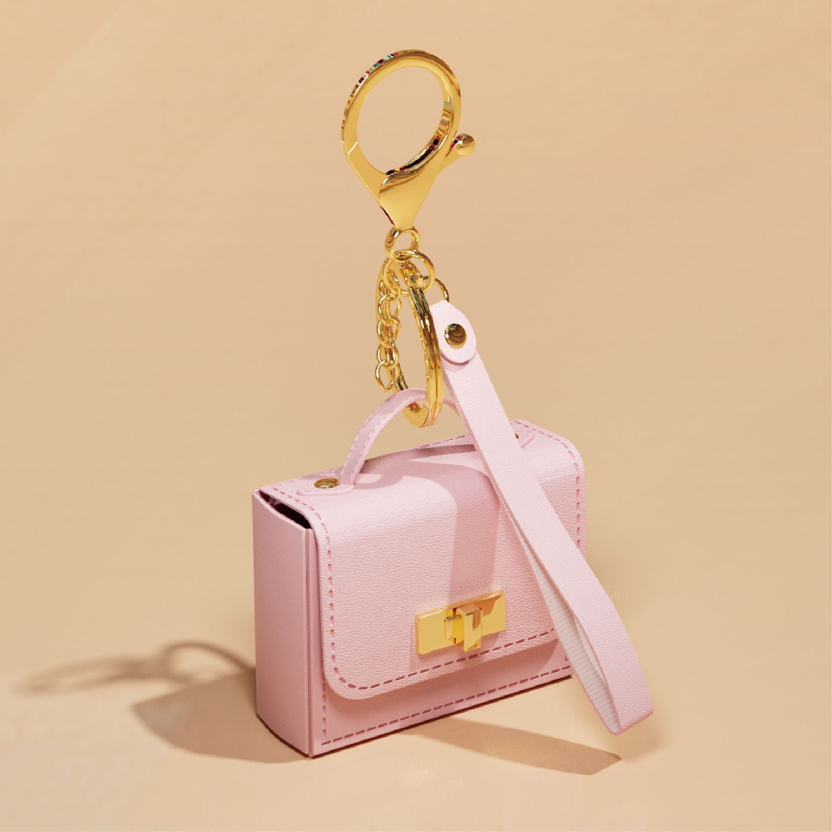 A miniature pink handbag-shaped keychain with a gold clasp, top handle, and a long matching pink strap attached to a gold key ring and chain, shown on a warm beige background.