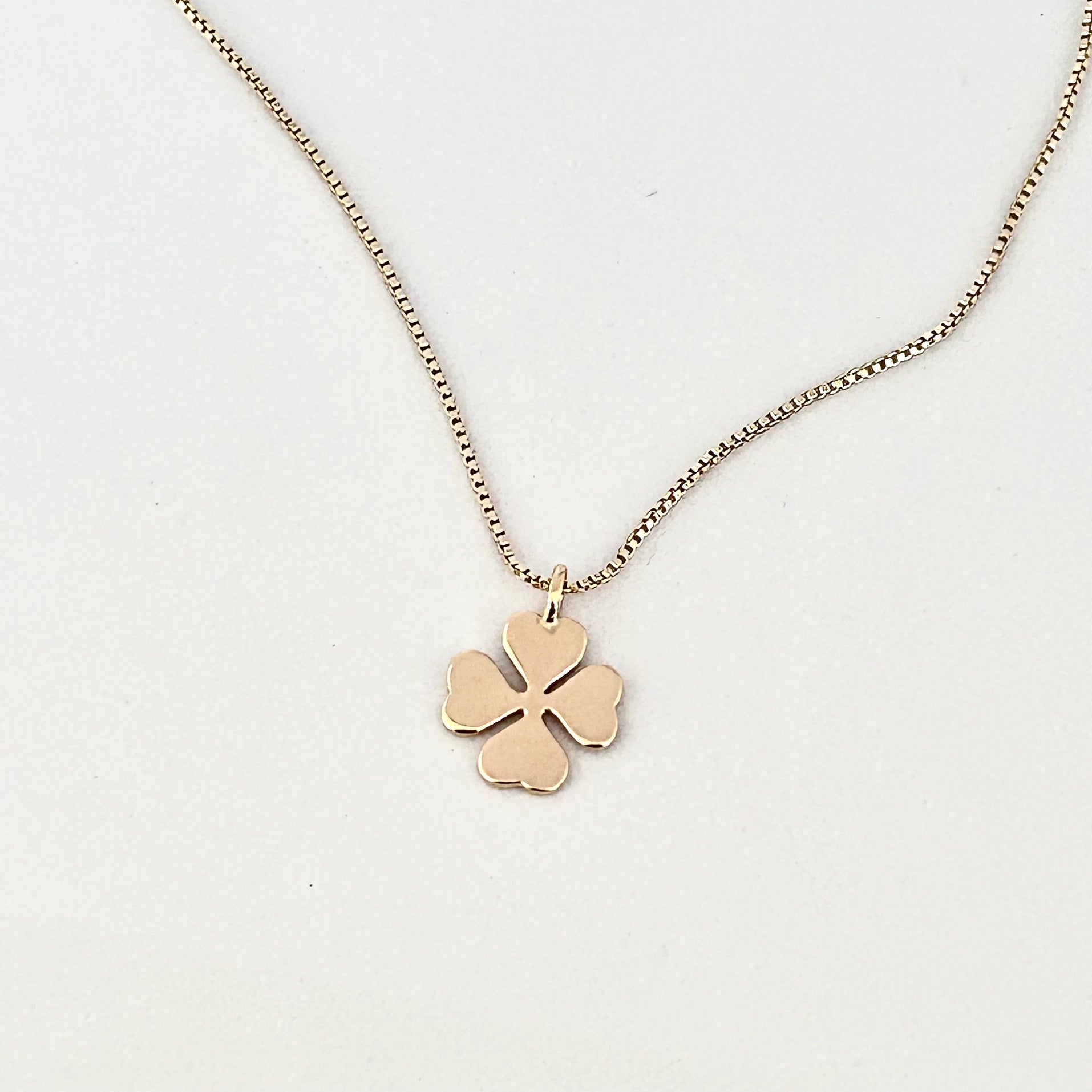 A delicate gold chain necklace featuring a small four-leaf clover pendant with a heart-shaped center, displayed on a clean white background.