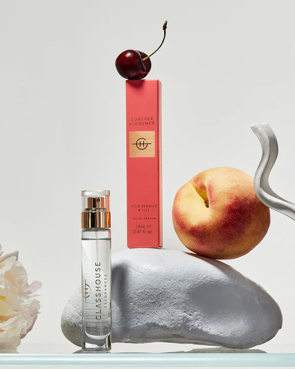 Perfume bottle, cherry, peach, and white flower on a light gray background